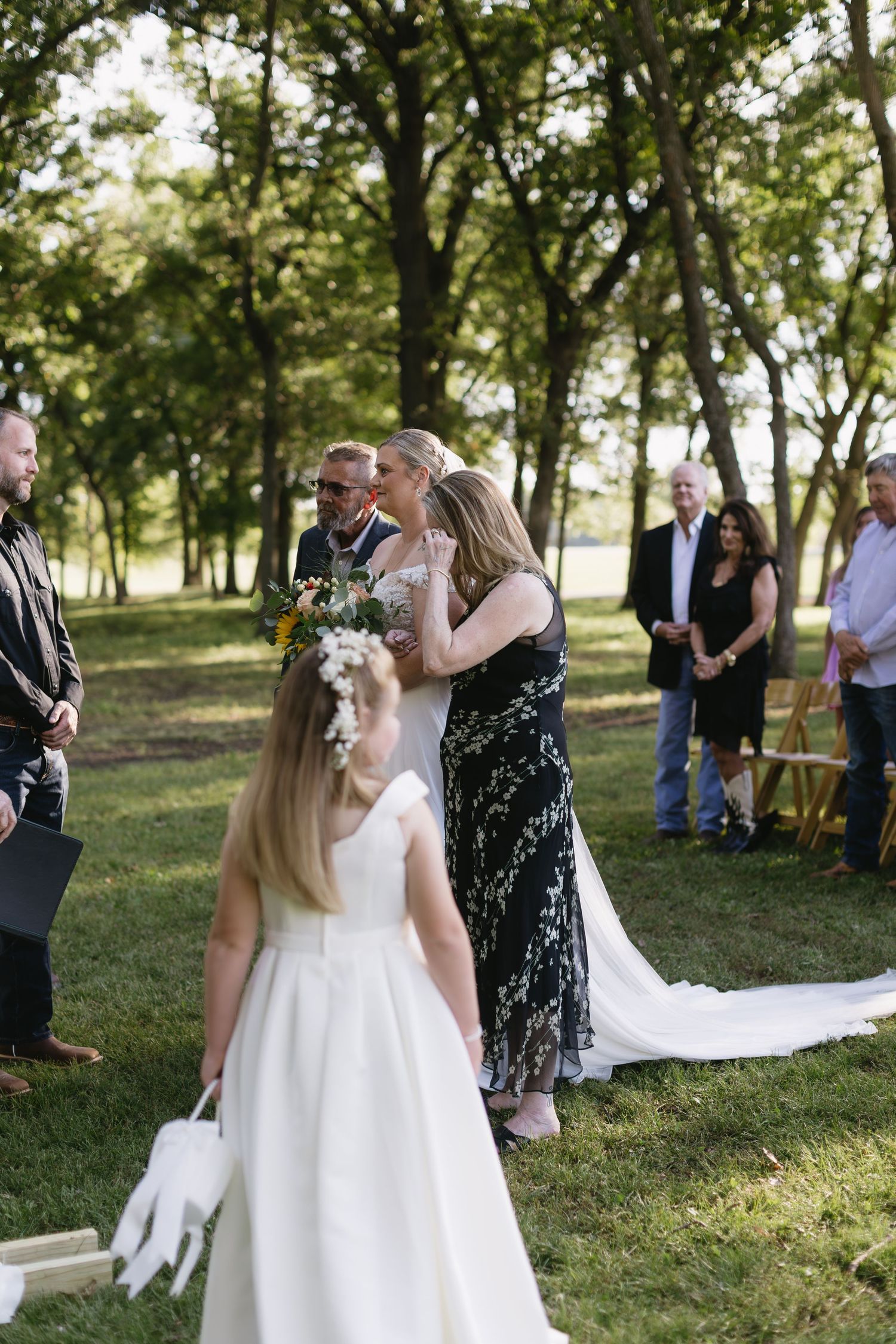 Outdoor wedding celebration with guests watching ceremony under trees.