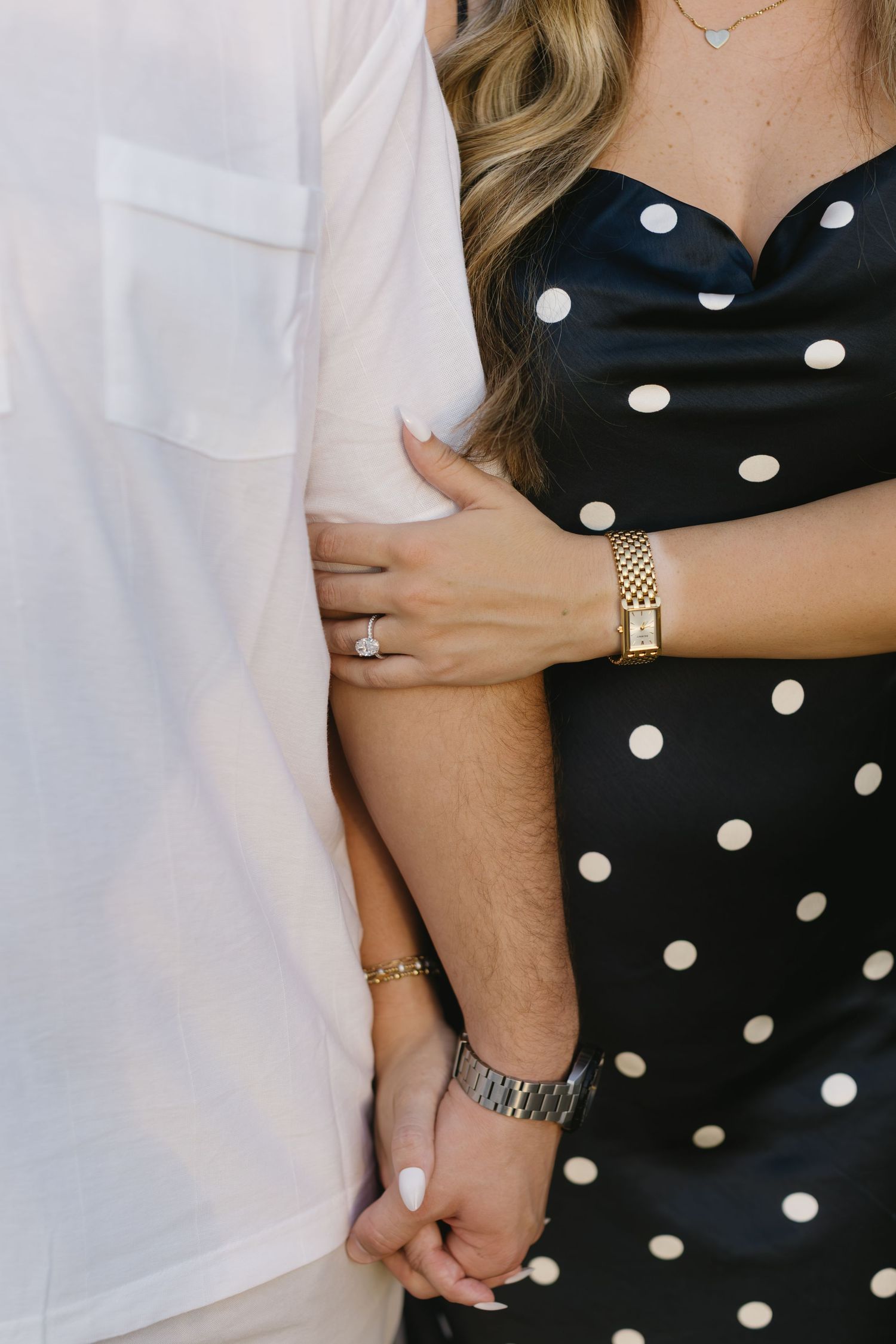 Close up detail shot of hands holding while wearing a navy polka dot dress and white shirt.