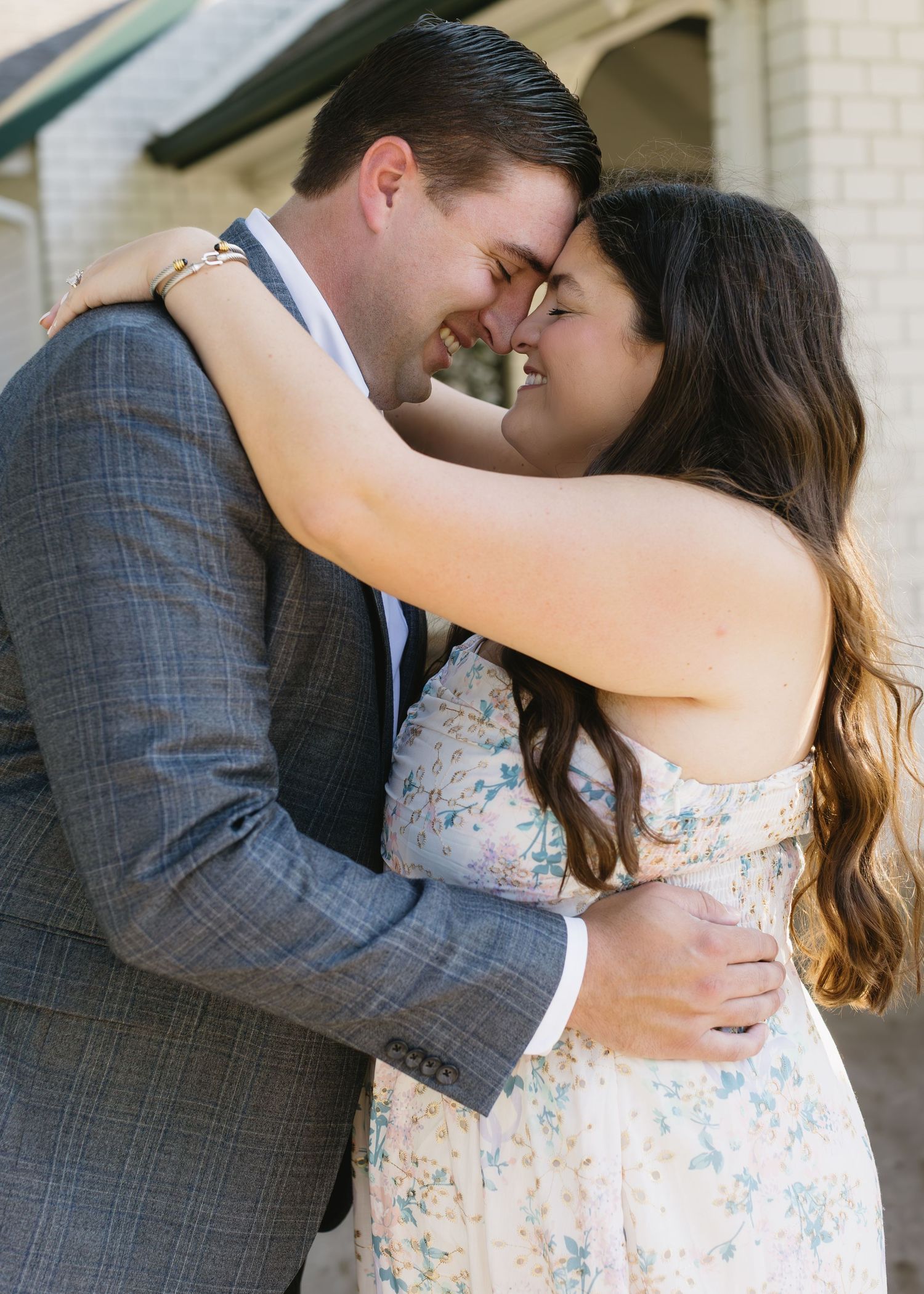 Romantic couple embracing while wearing formal attire against a brick wall background.