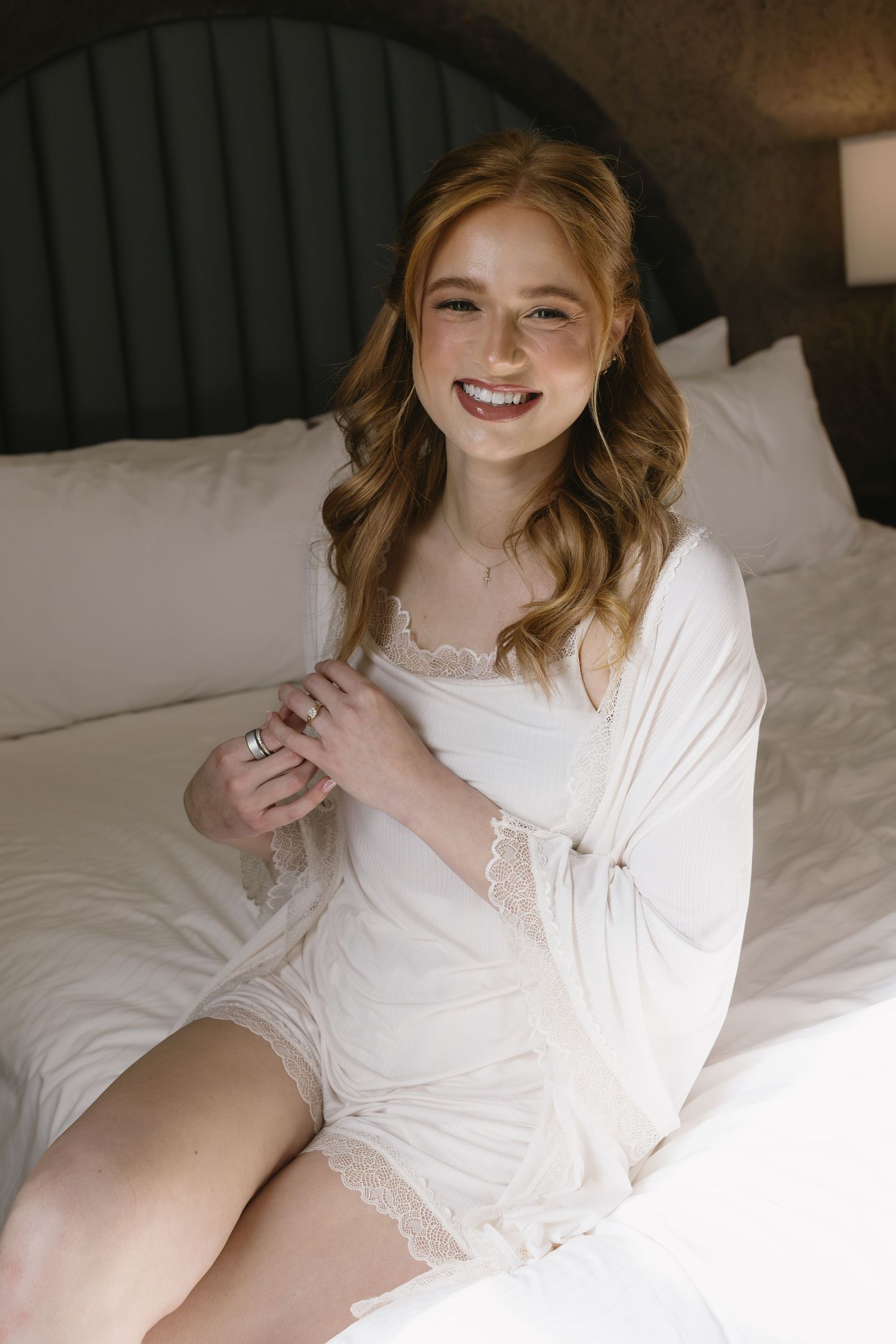 Intimate bridal boudoir photography session featuring white lace robe on white bedding.
