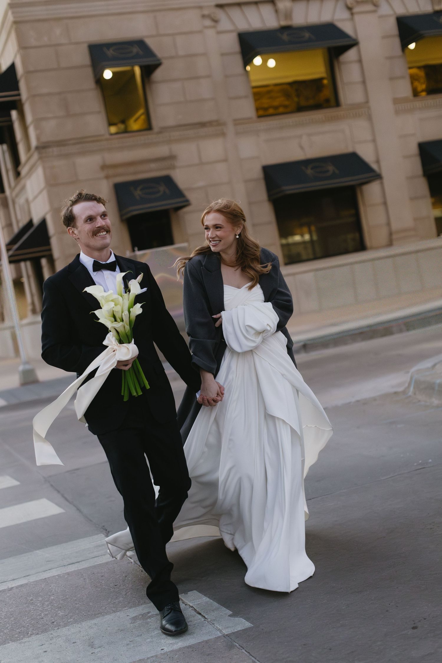 Playful wedding couple dancing and twirling on an urban street with classic architecture.