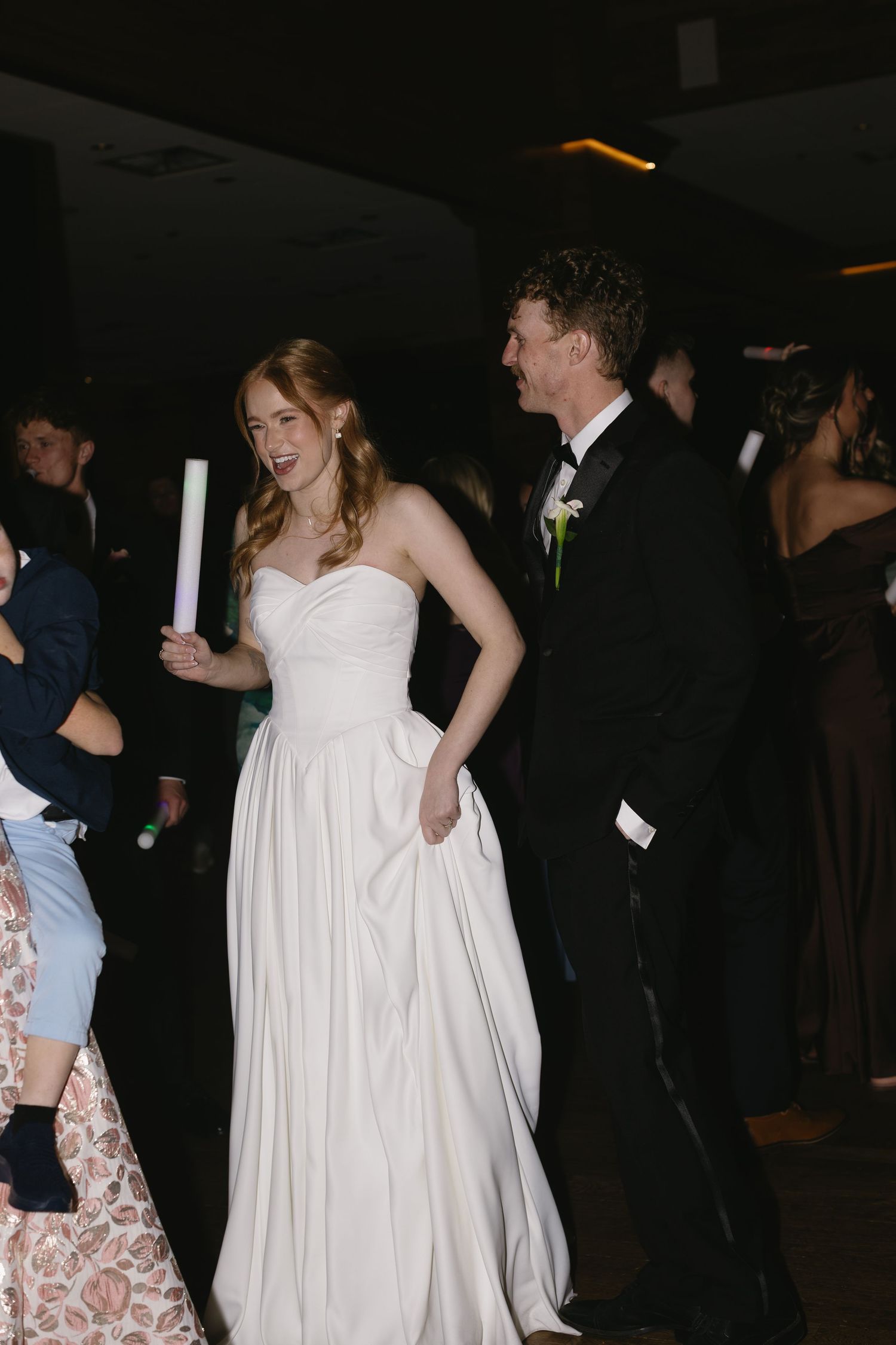 Wedding reception guests dance and celebrate on a dimly lit dance floor.