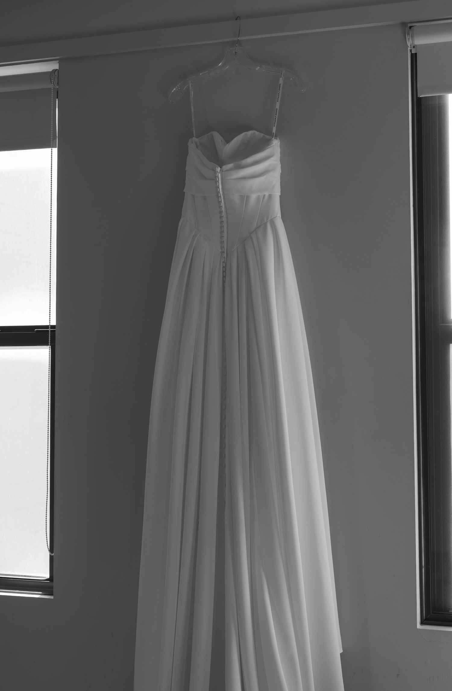 White wedding dresses hanging in a row against a gray wall with natural window light.