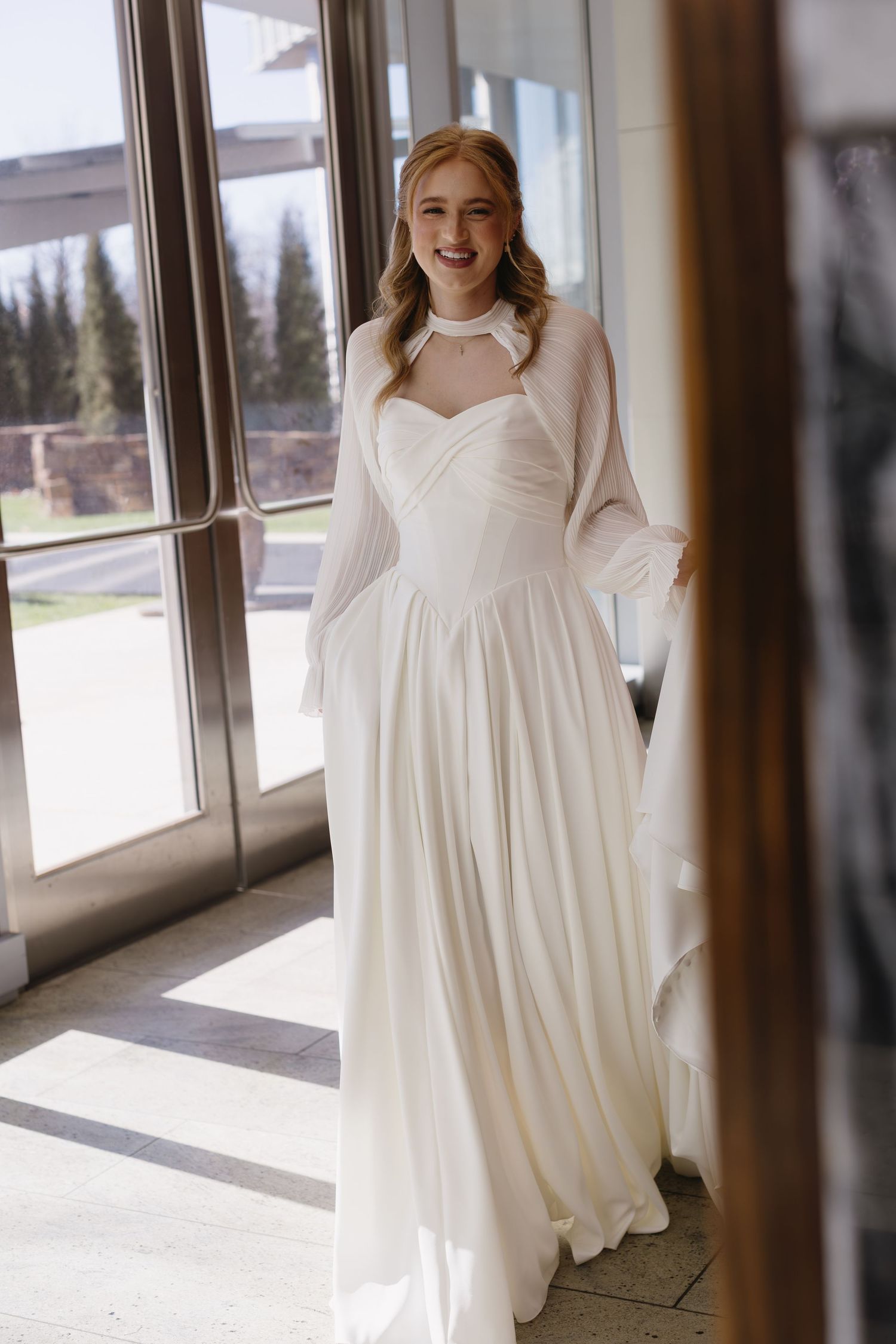 Elegant white wedding dress with flowing fabric shown in multiple angles against a bright window backdrop.