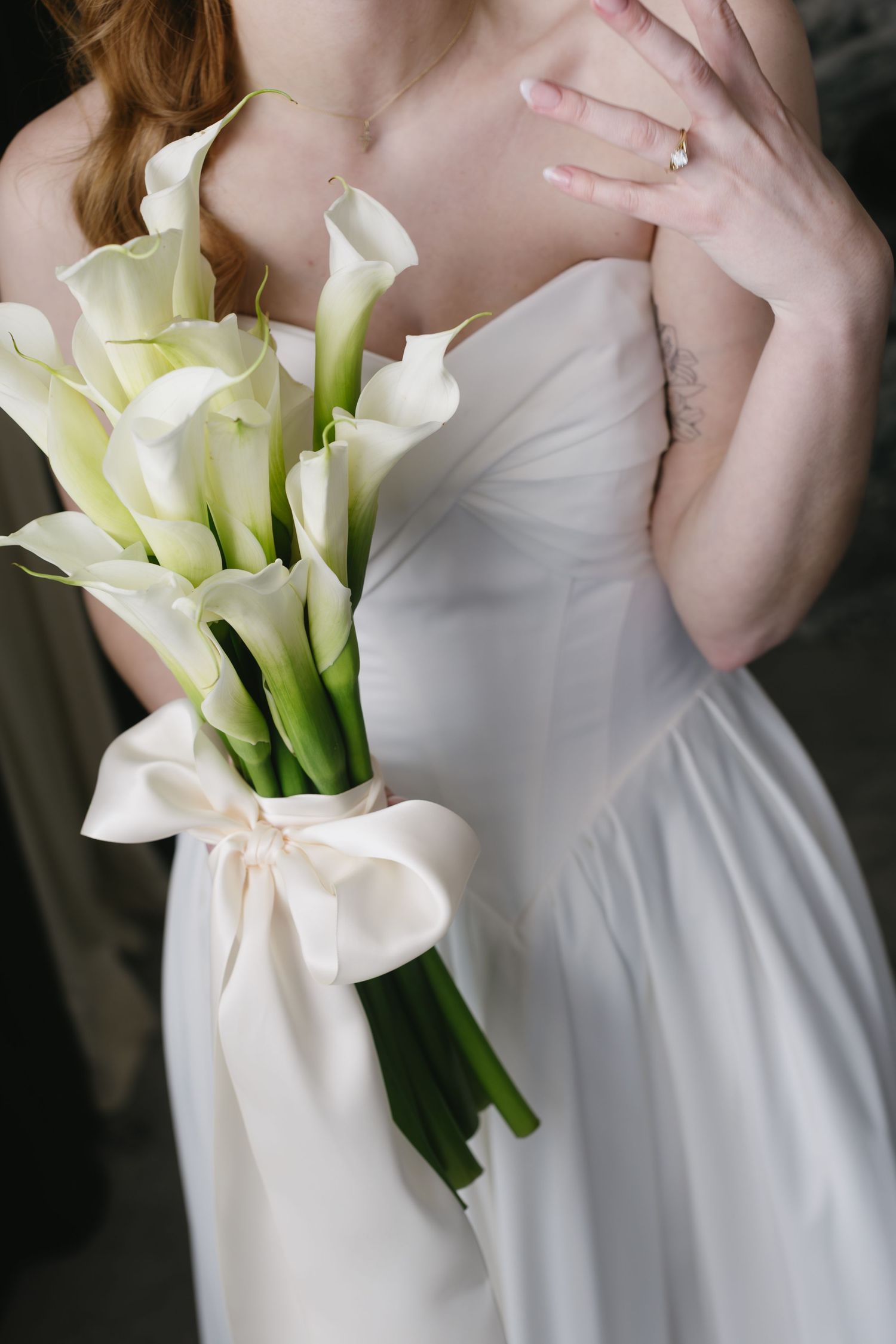 Elegant white wedding dress detail with a bouquet of fresh white calla lilies.