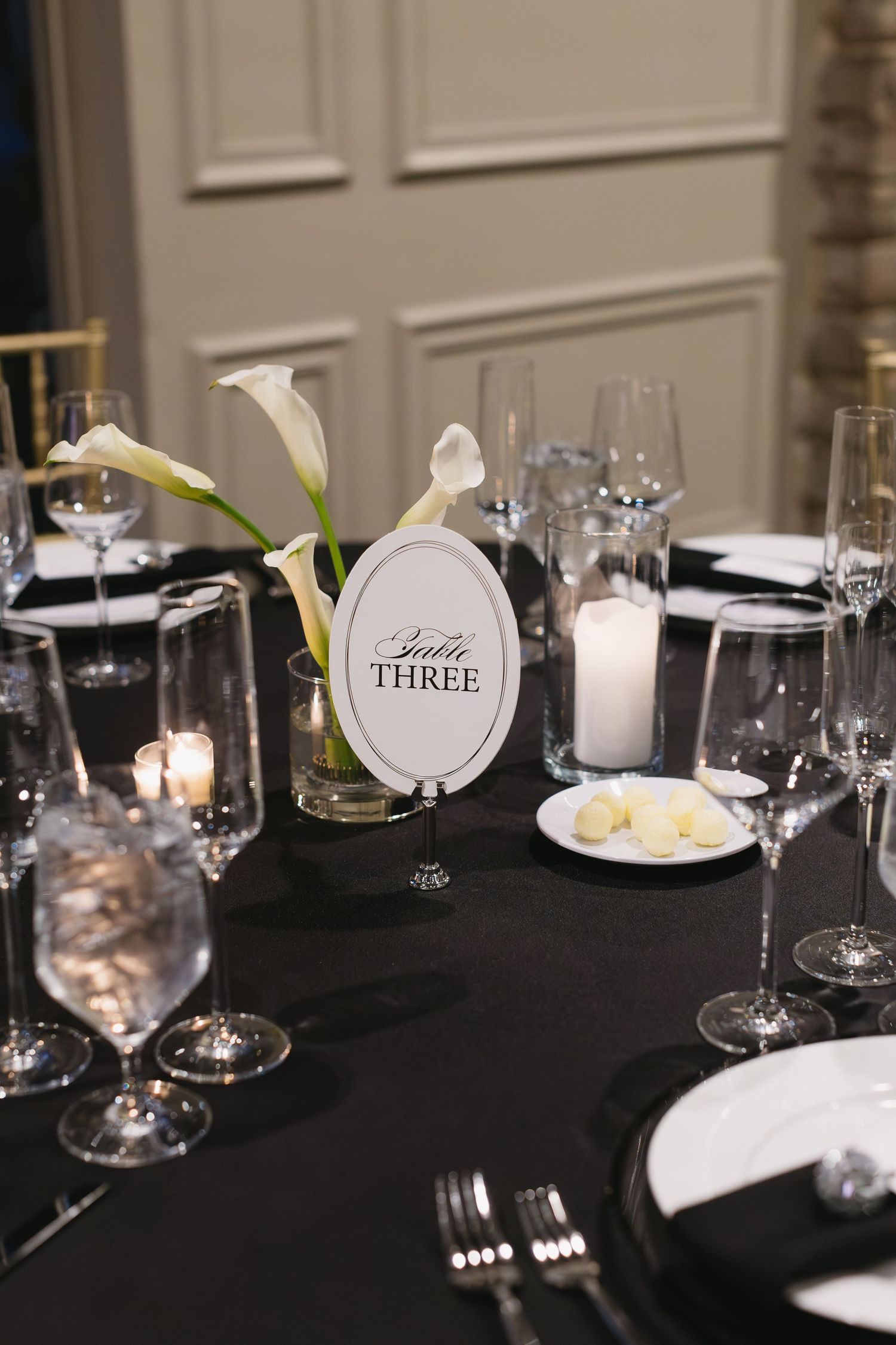 Formal table setting with black tablecloth, wine glasses, and white floral centerpieces.