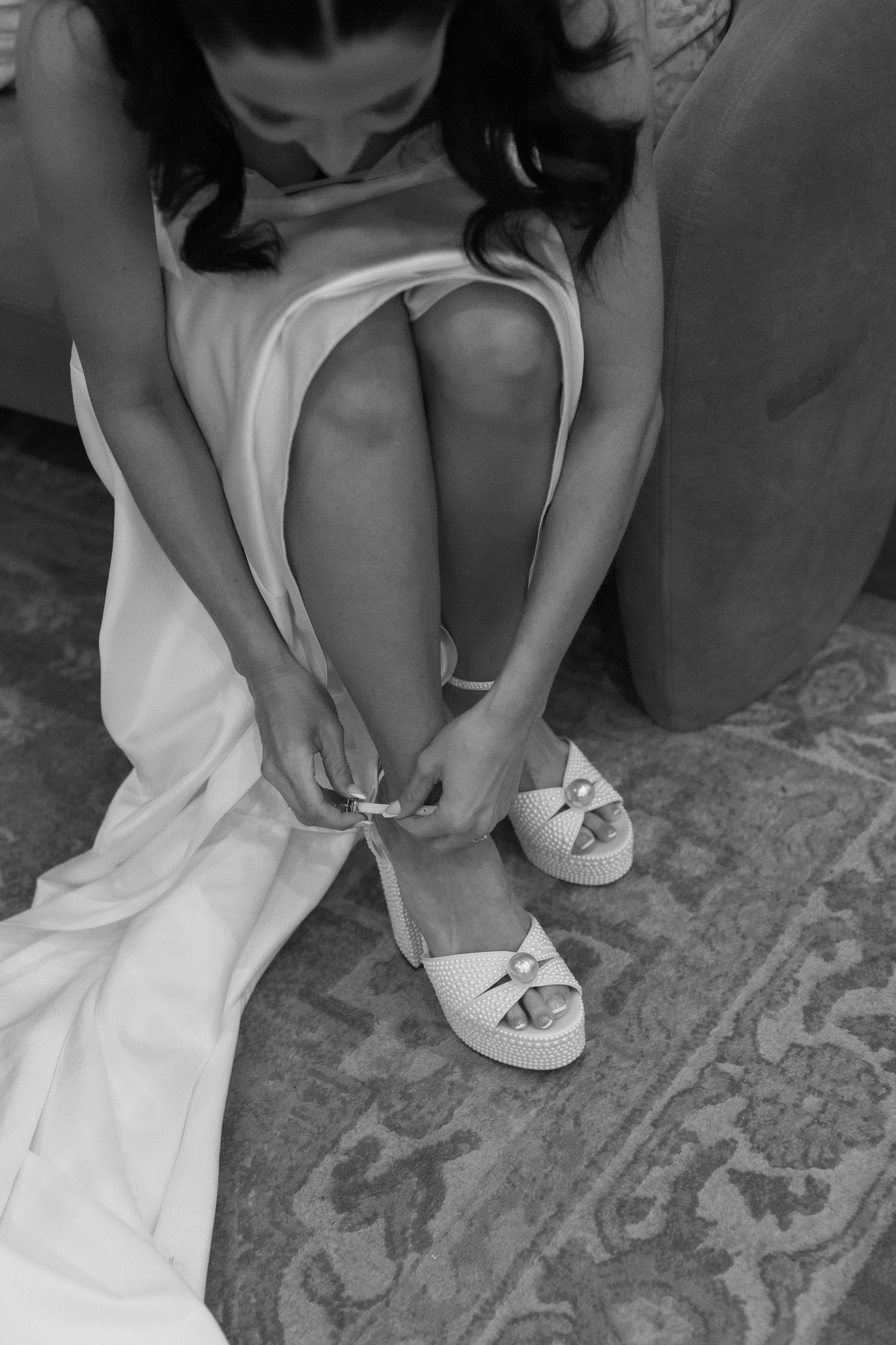 Black and white photo of someone fastening delicate bridal shoes.