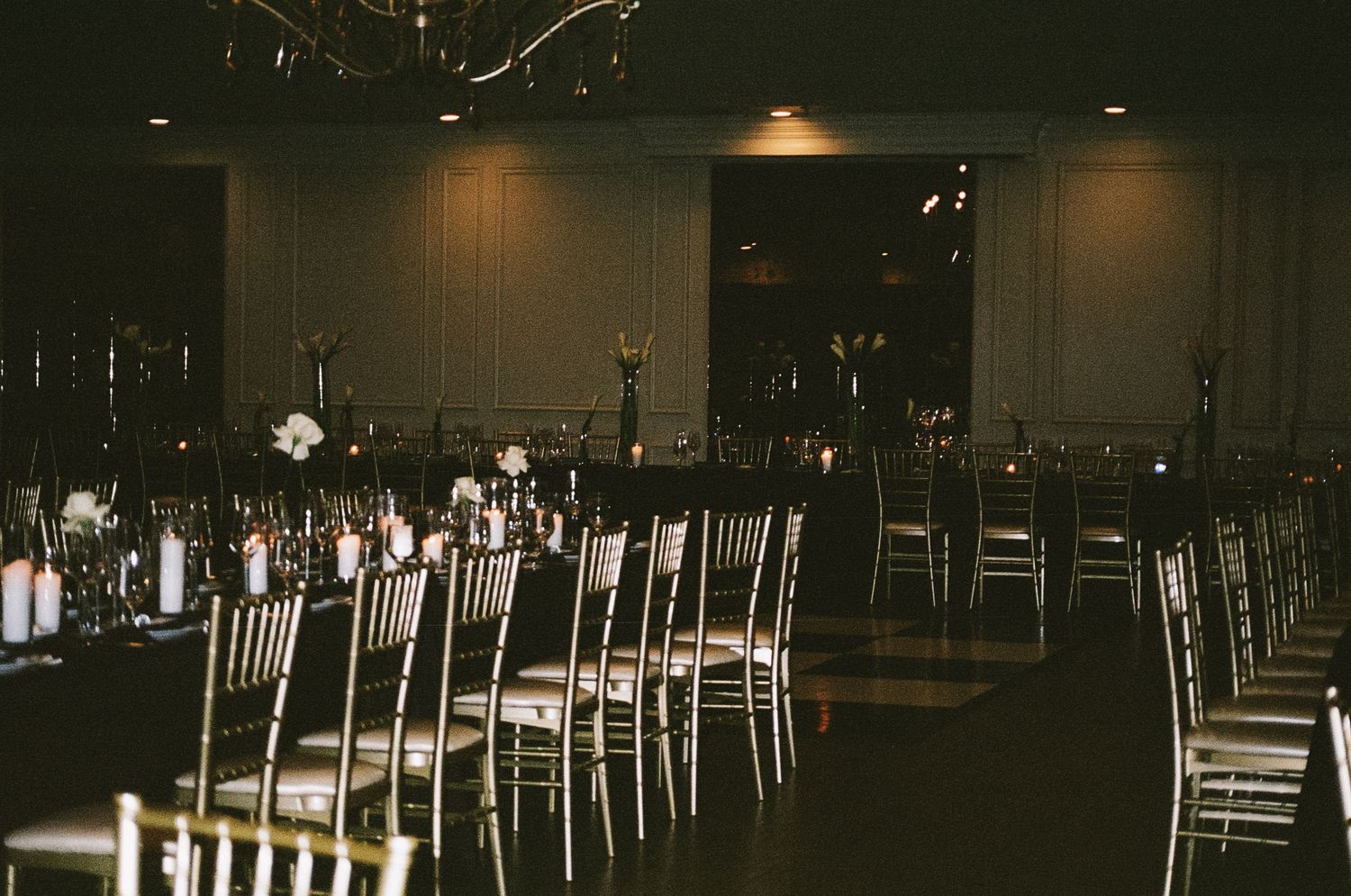 Dark reception hall with white chairs arranged in rows for wedding ceremony.