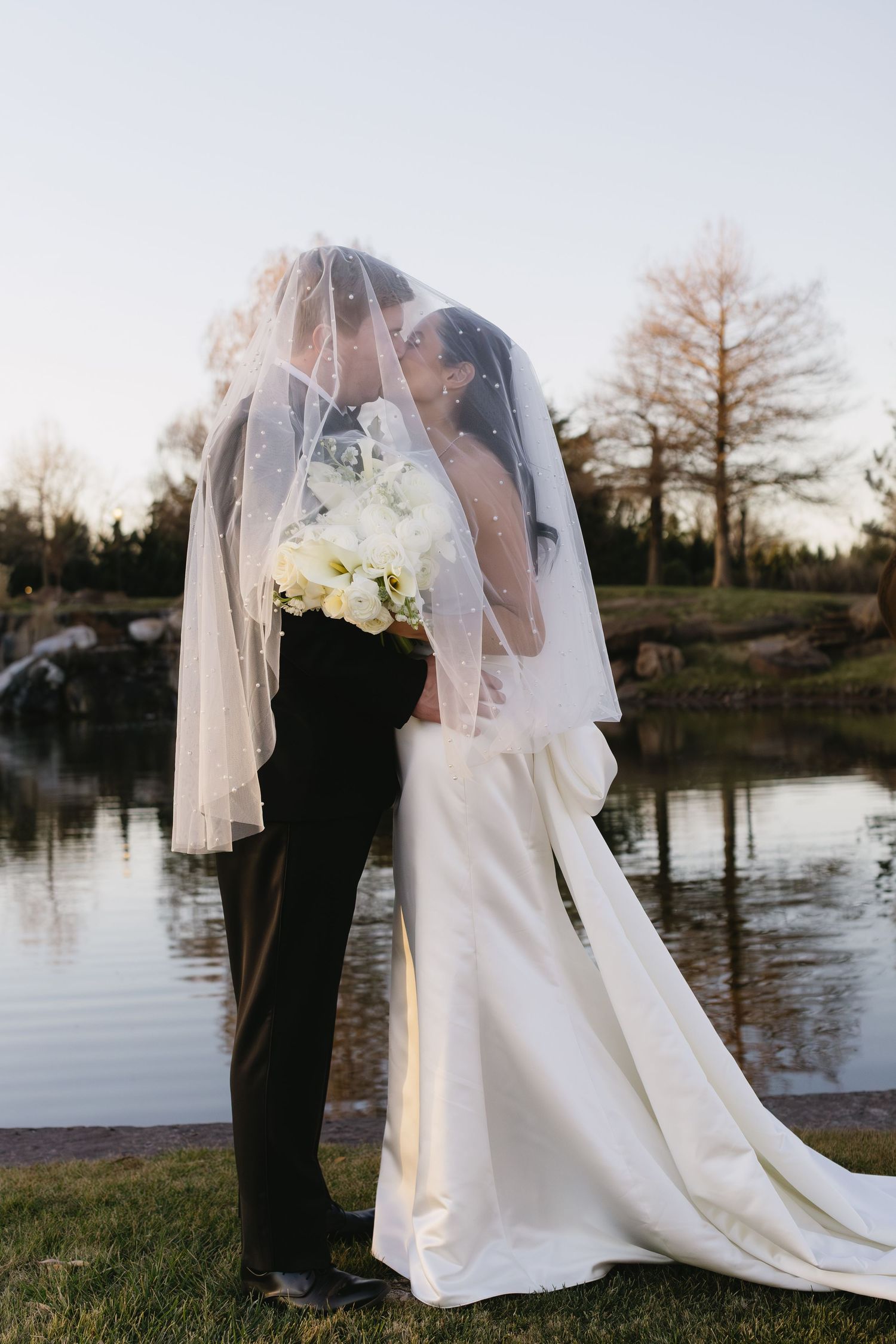 Romantic waterfront wedding portraits with bride's veil flowing in evening light.