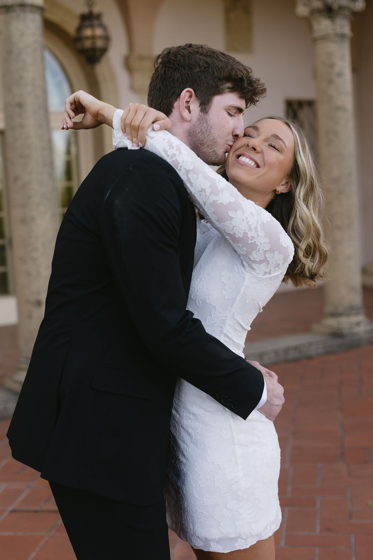 A romantic wedding couple embraces and dances together in a columned courtyard.