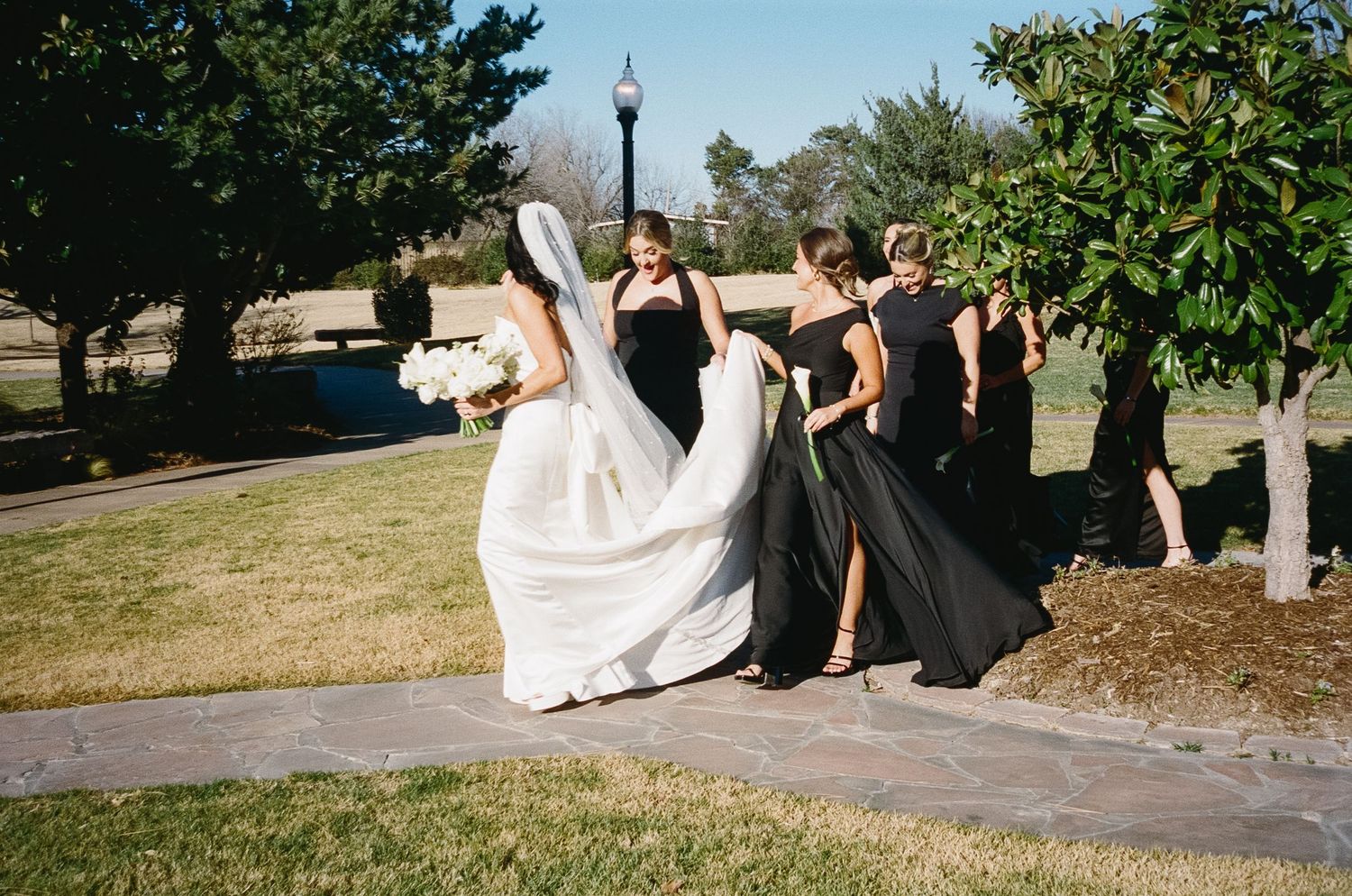 Wedding party walking together on a sunny path with flowing dresses in black and white.