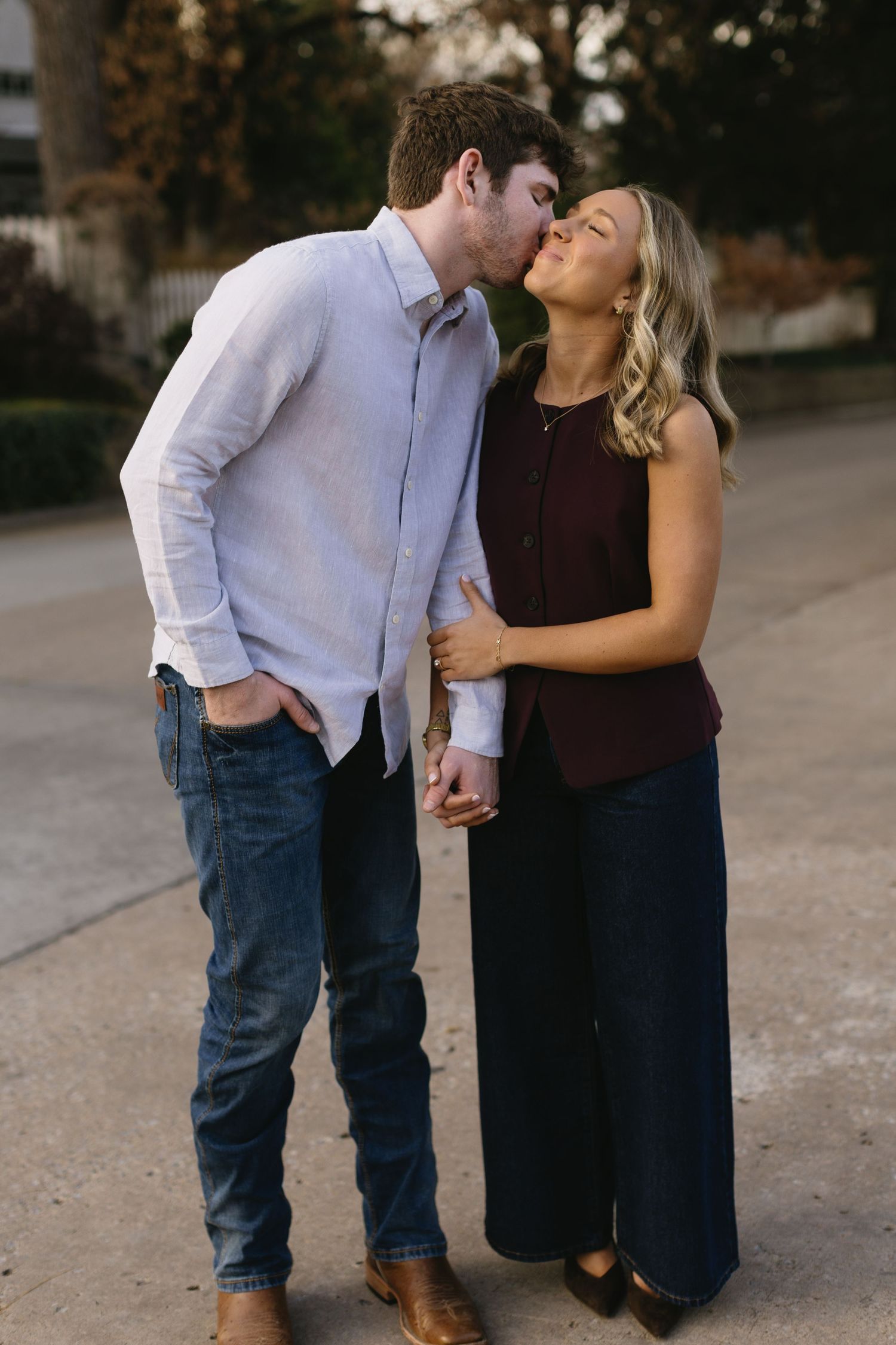 A romantic couple shares intimate moments in casual attire on a walkway at dusk.