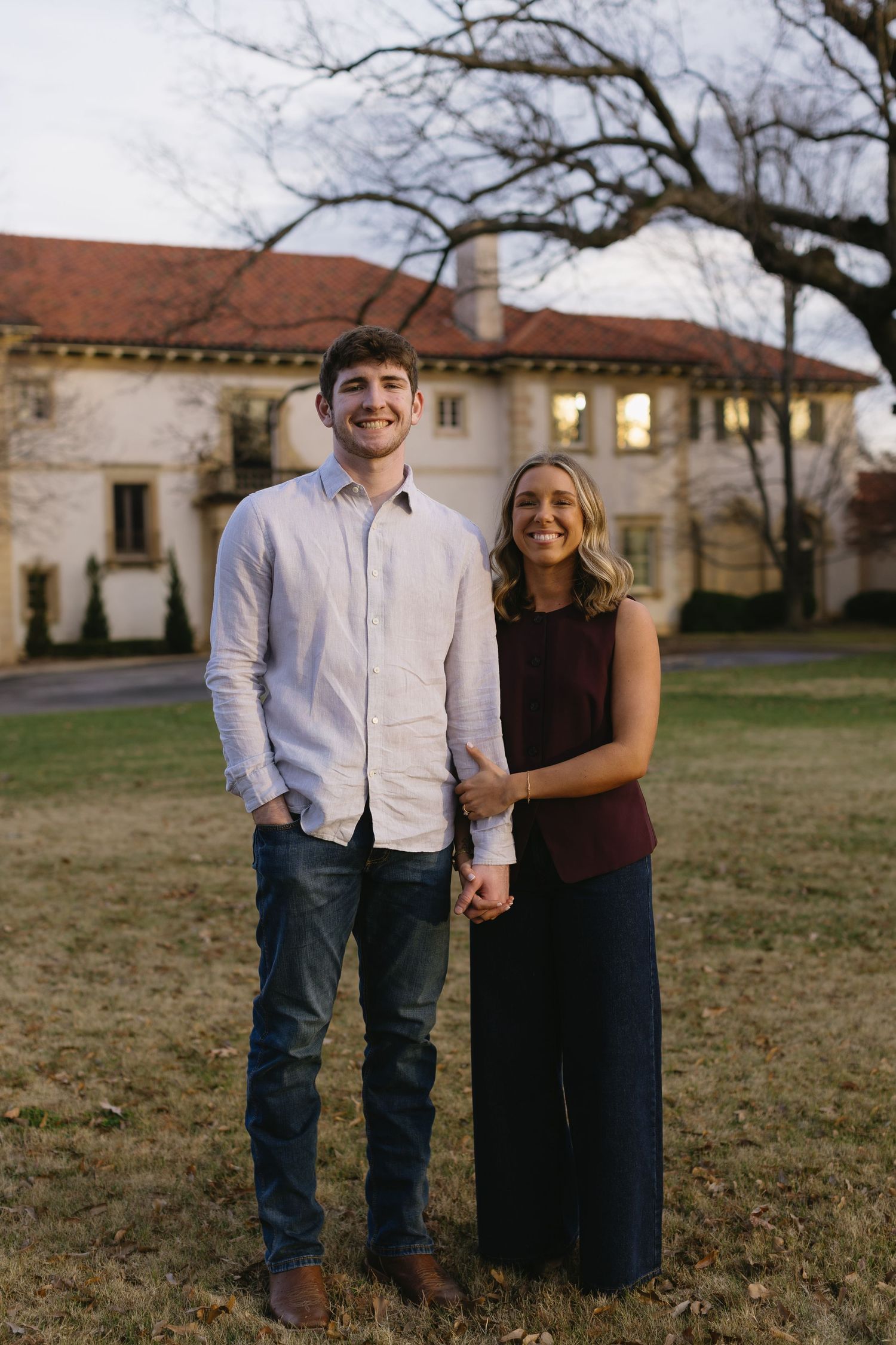 A couple poses together on a lawn with Spanish-style architecture visible in the background.