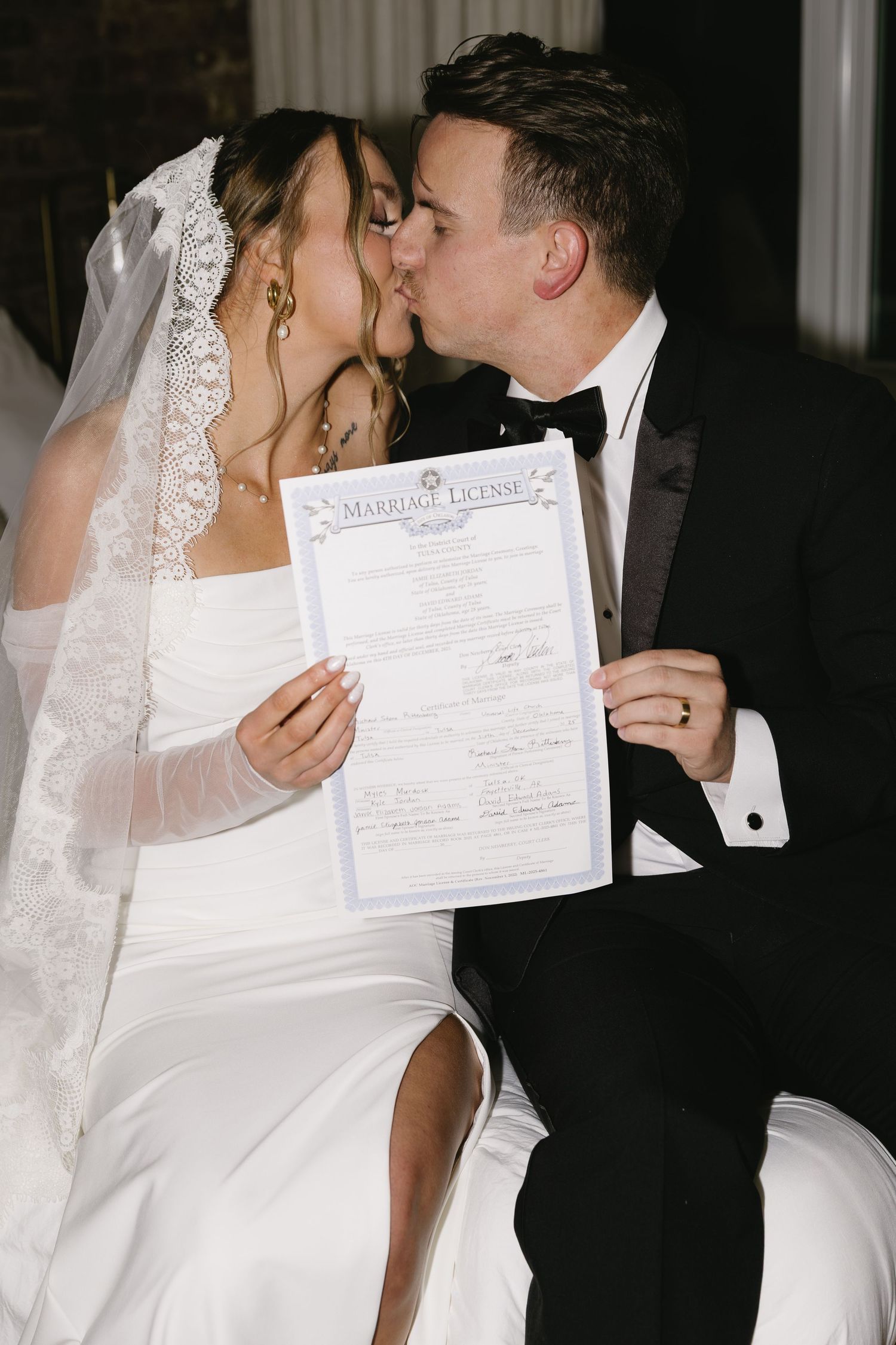 A newlywed couple sharing a kiss while holding their marriage certificate.