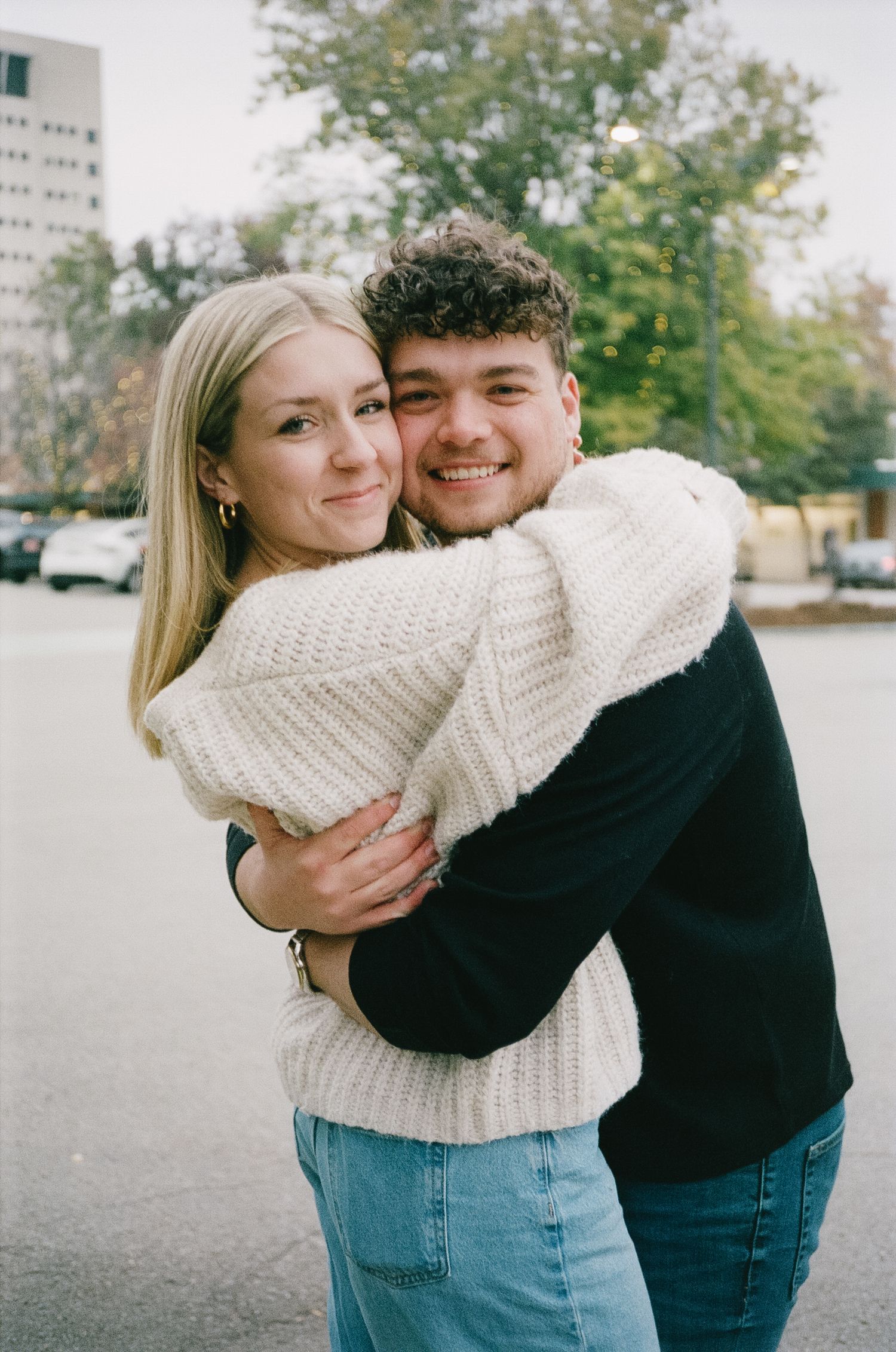 A couple in casual attire sharing a warm embrace outdoors on an autumn day.