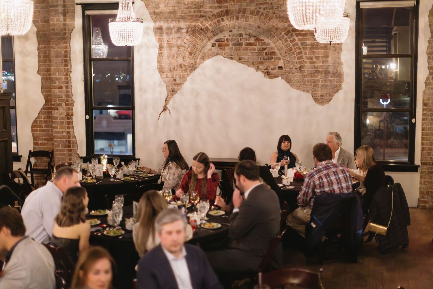 Guests mingling at social gathering in rustic brick-walled venue with pendant lighting.