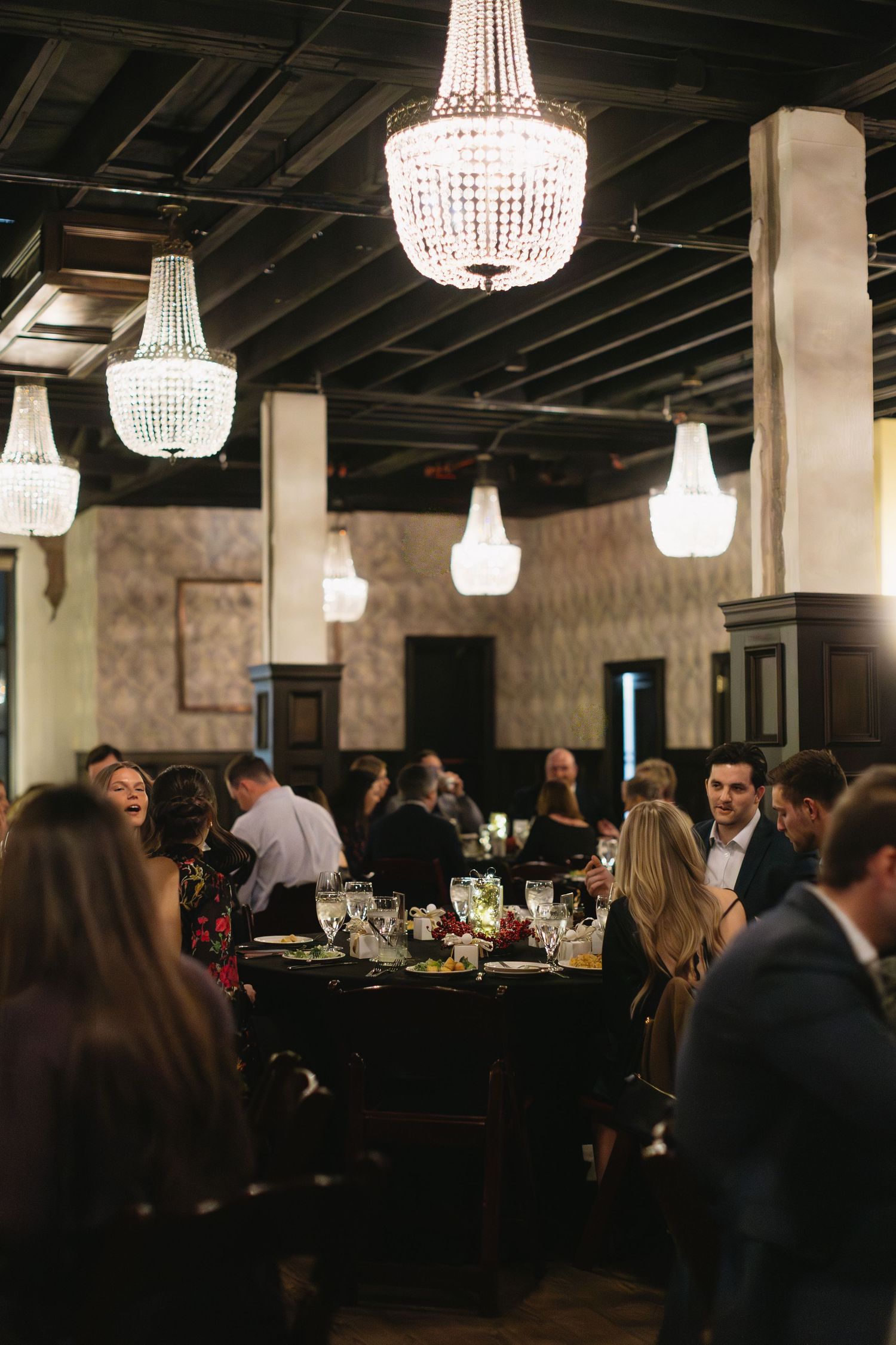 Elegant reception venue with crystal chandeliers illuminating a dark industrial-style space.