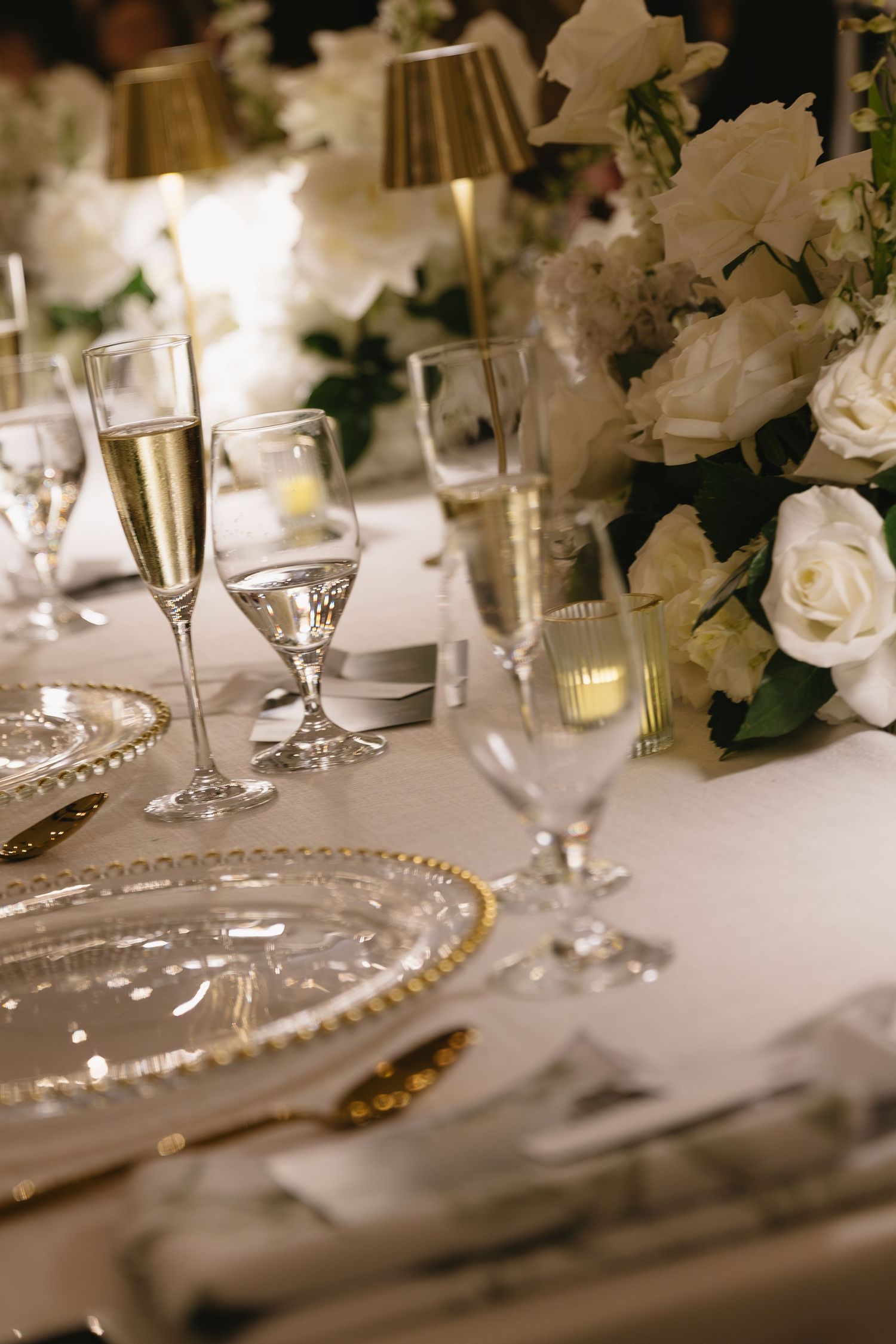 An elegant table setting with champagne flutes, crystal glasses, and white rose centerpieces.