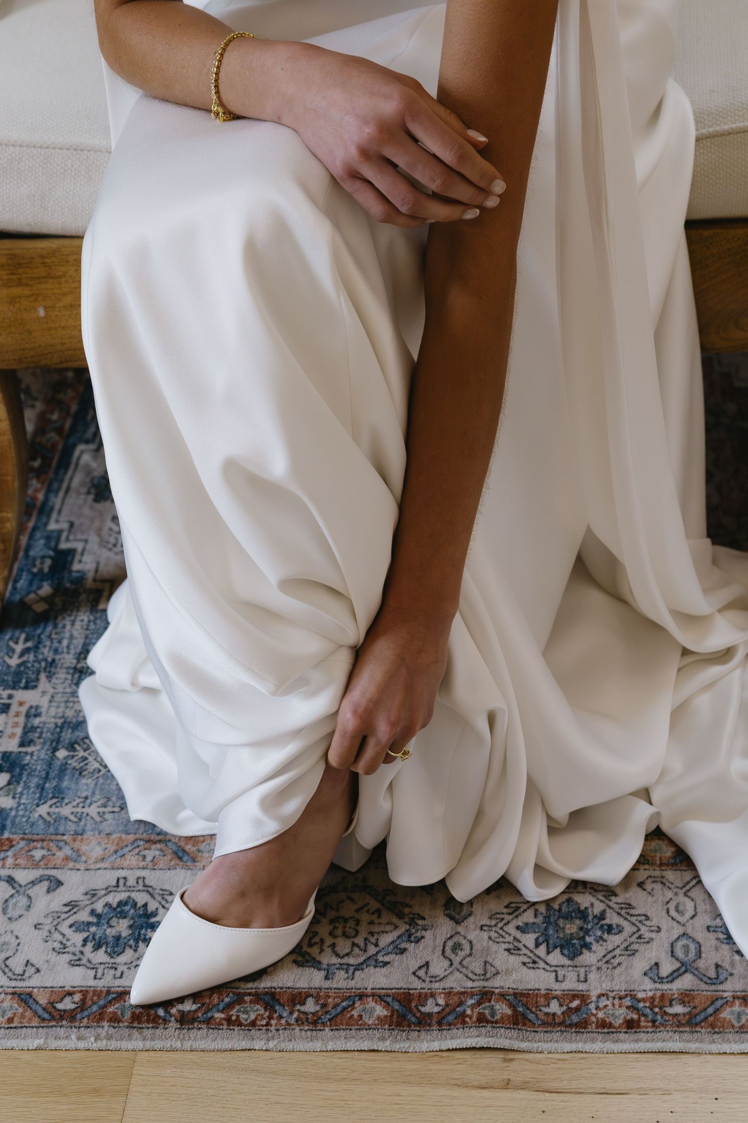 Detail shot of white wedding dress hem and shoes on vintage patterned rug.