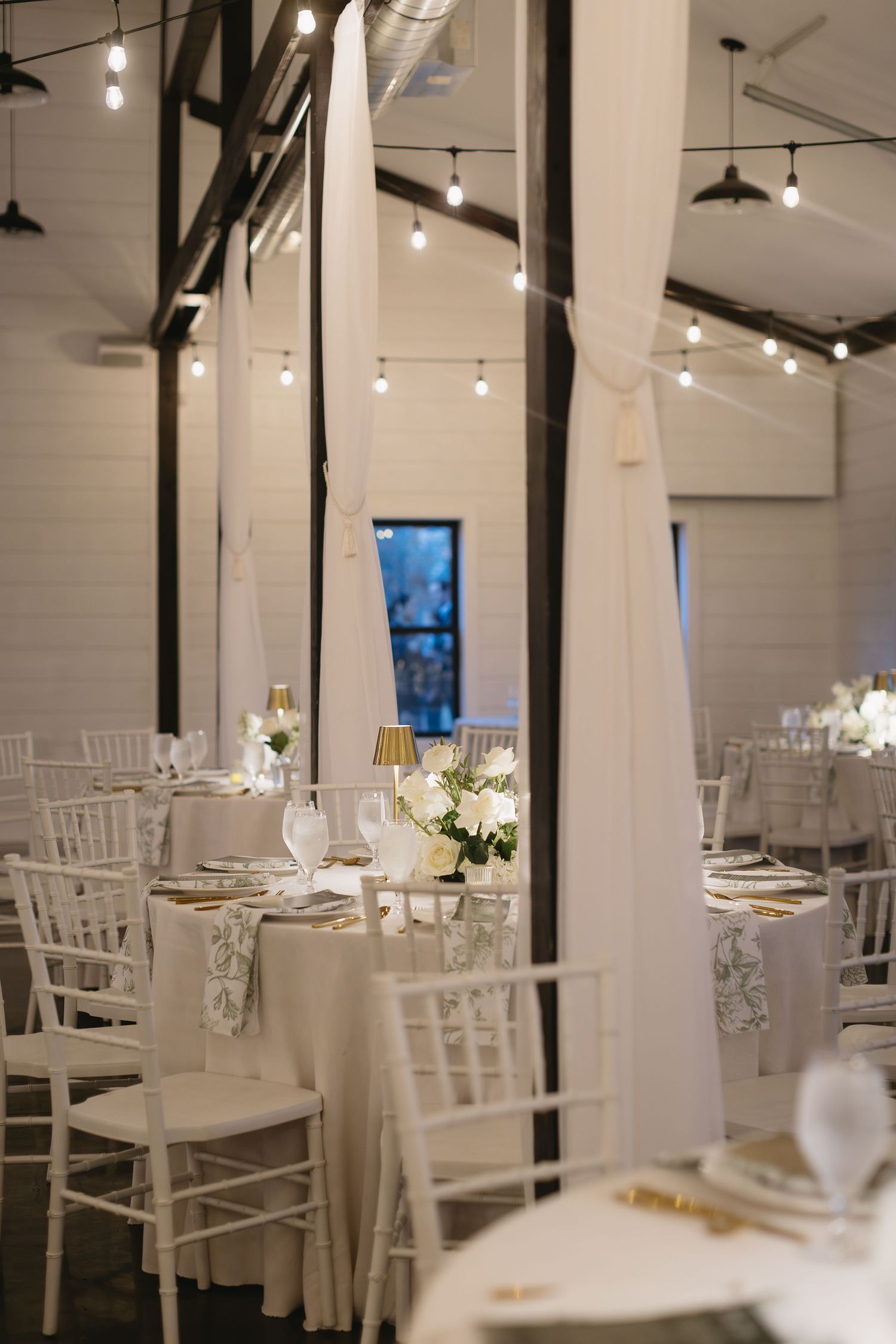 Modern white wedding venue with string lights and elegant table settings.