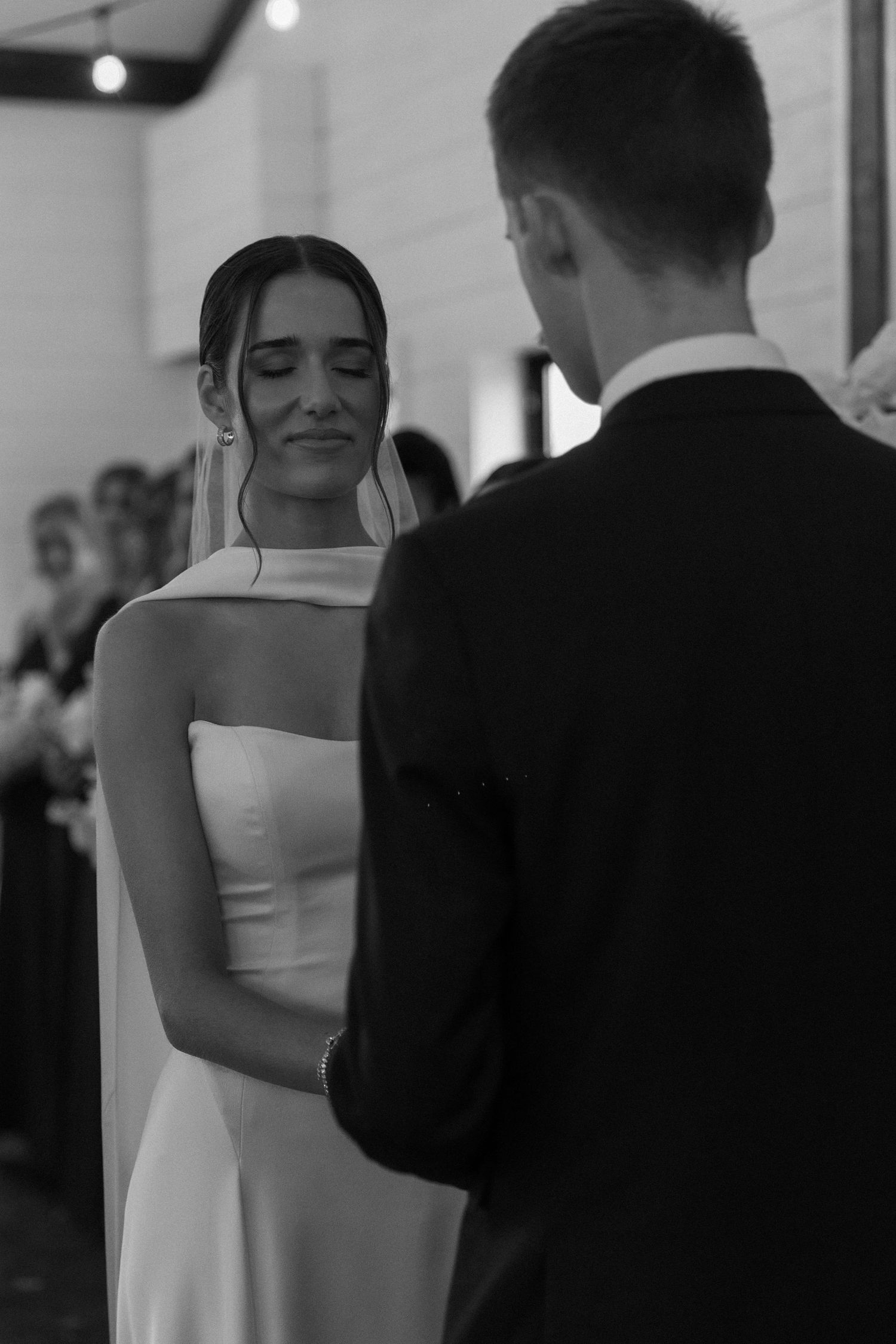 Black and white photo of couple exchanging vows during intimate indoor ceremony.