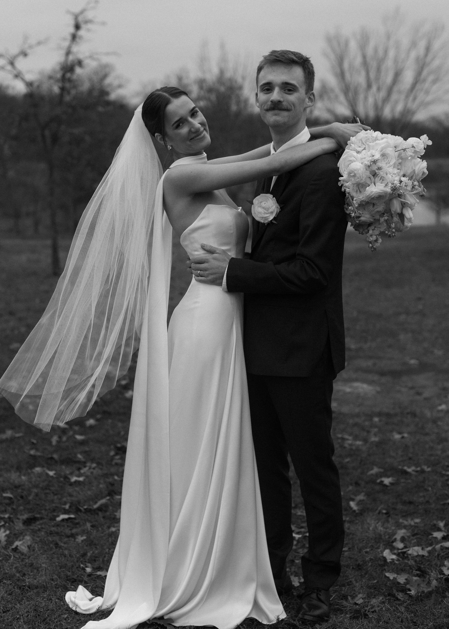 Black and white photo of wedding couple dancing outdoors in autumn.