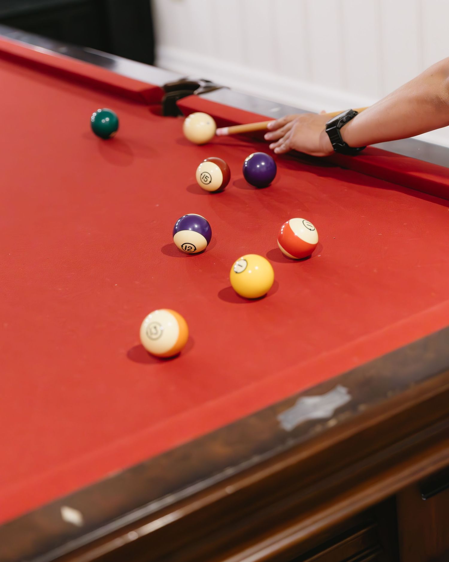 Several colorful billiard balls scattered on a red pool table with a hand holding a cue stick.