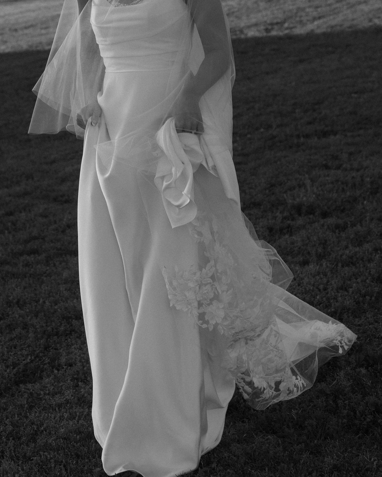 Black and white photo of flowing wedding dress fabric moving in the wind against dark background.