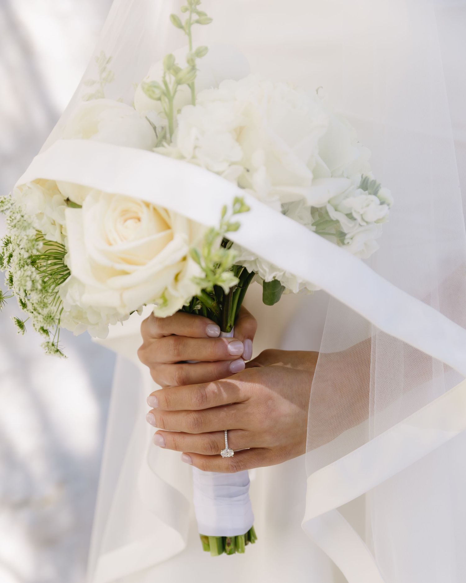 Close-up of delicate white rose wedding bouquet being held with an engagement ring visible.