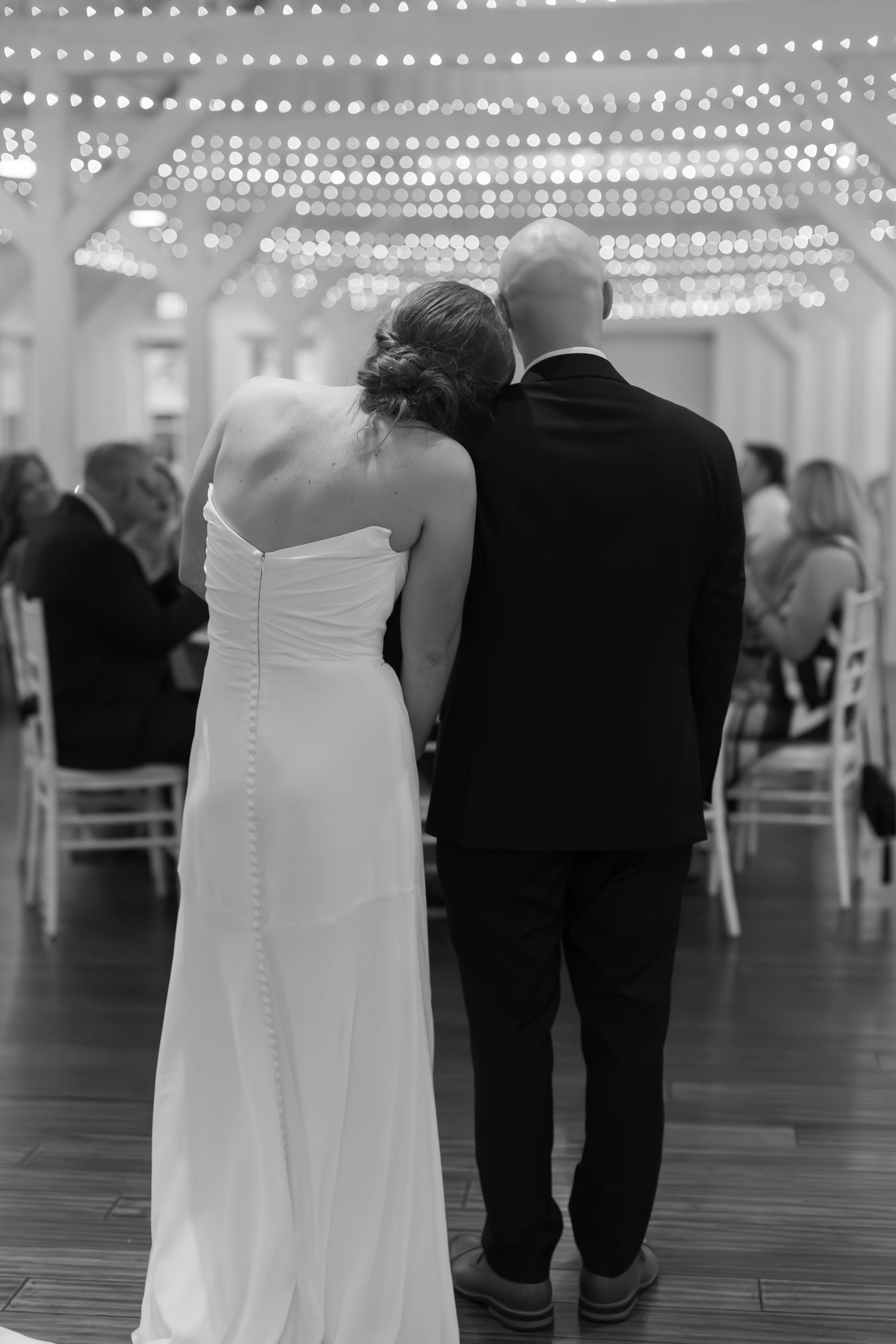 Black and white photo of a couple under twinkling string lights at their wedding reception.