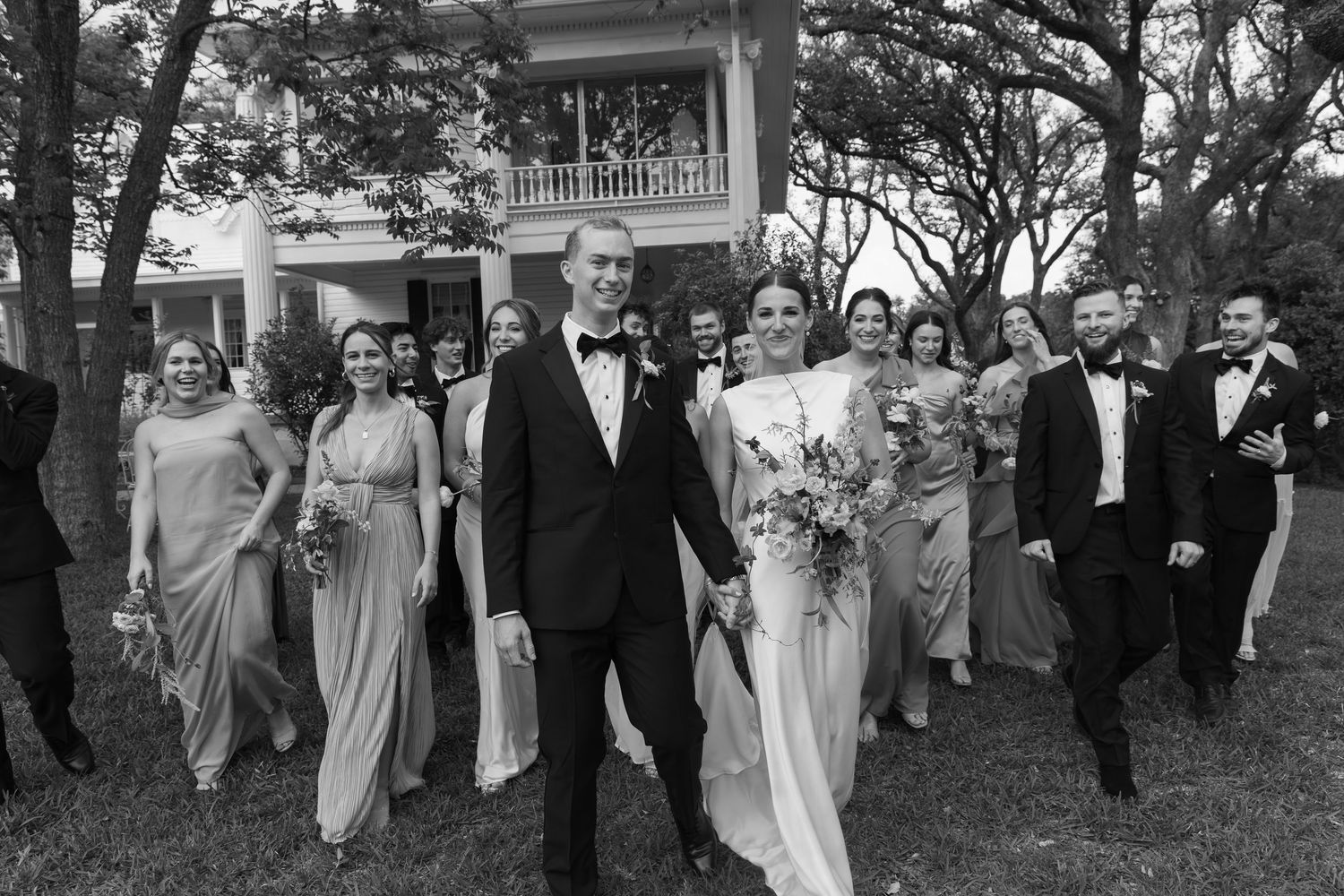 Wedding party in formal attire walking together outdoors in black and white.