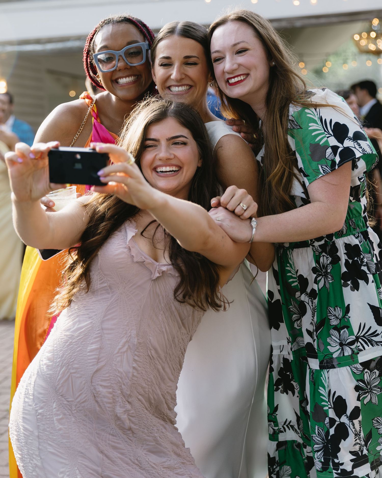 Joyful wedding celebration with attendees in colorful floral dresses sharing embraces and laughter.