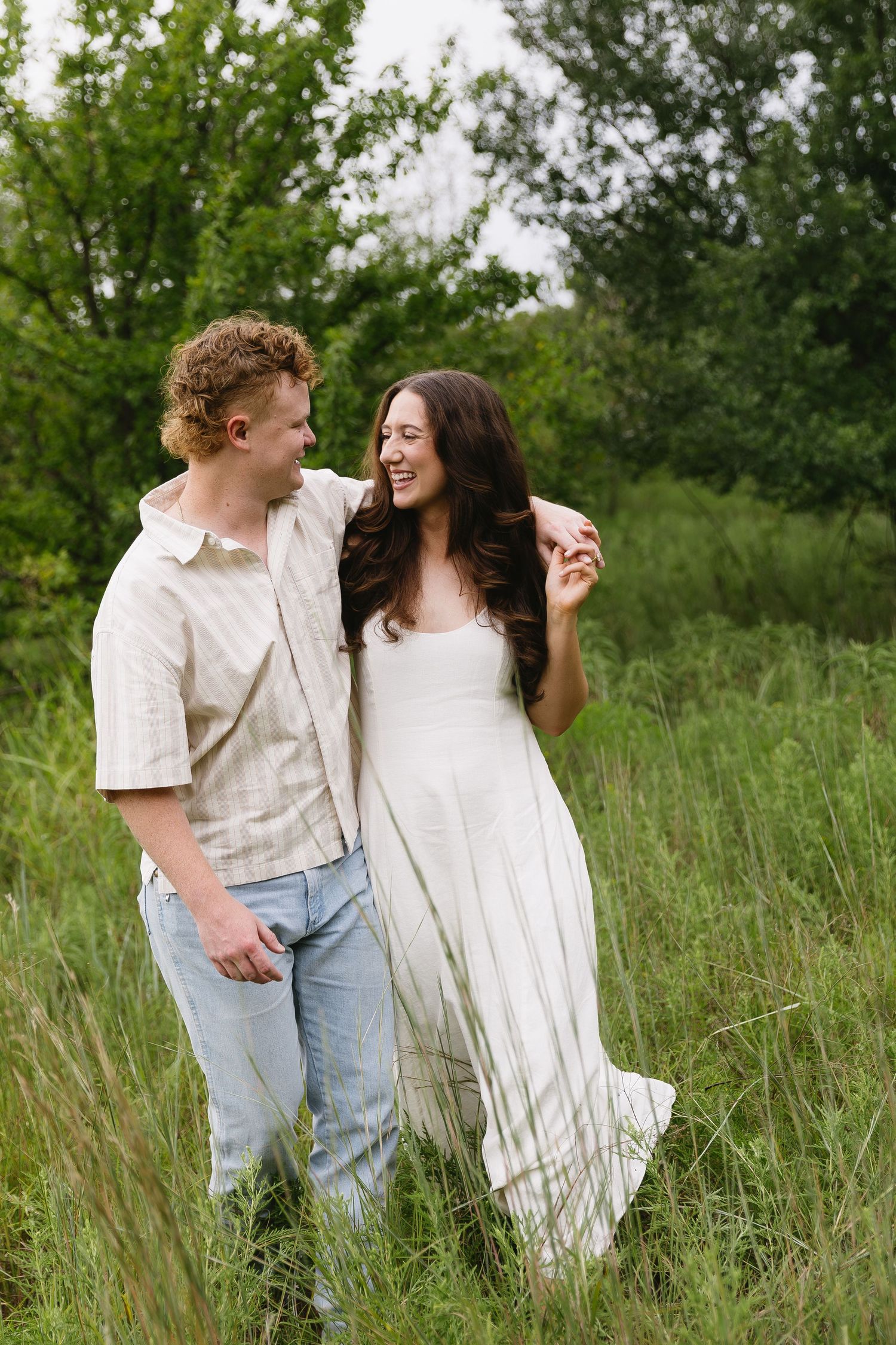 A joyful couple walks through a sunlit meadow wearing white and light colored clothing.