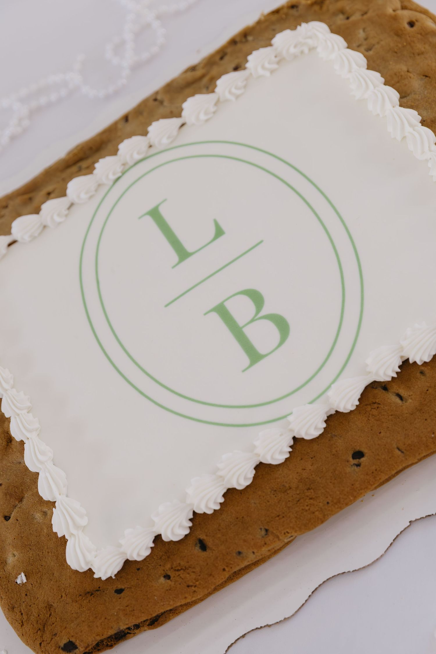 Close-up view of decorative monogram letters in light green on white scalloped paper against brown background.