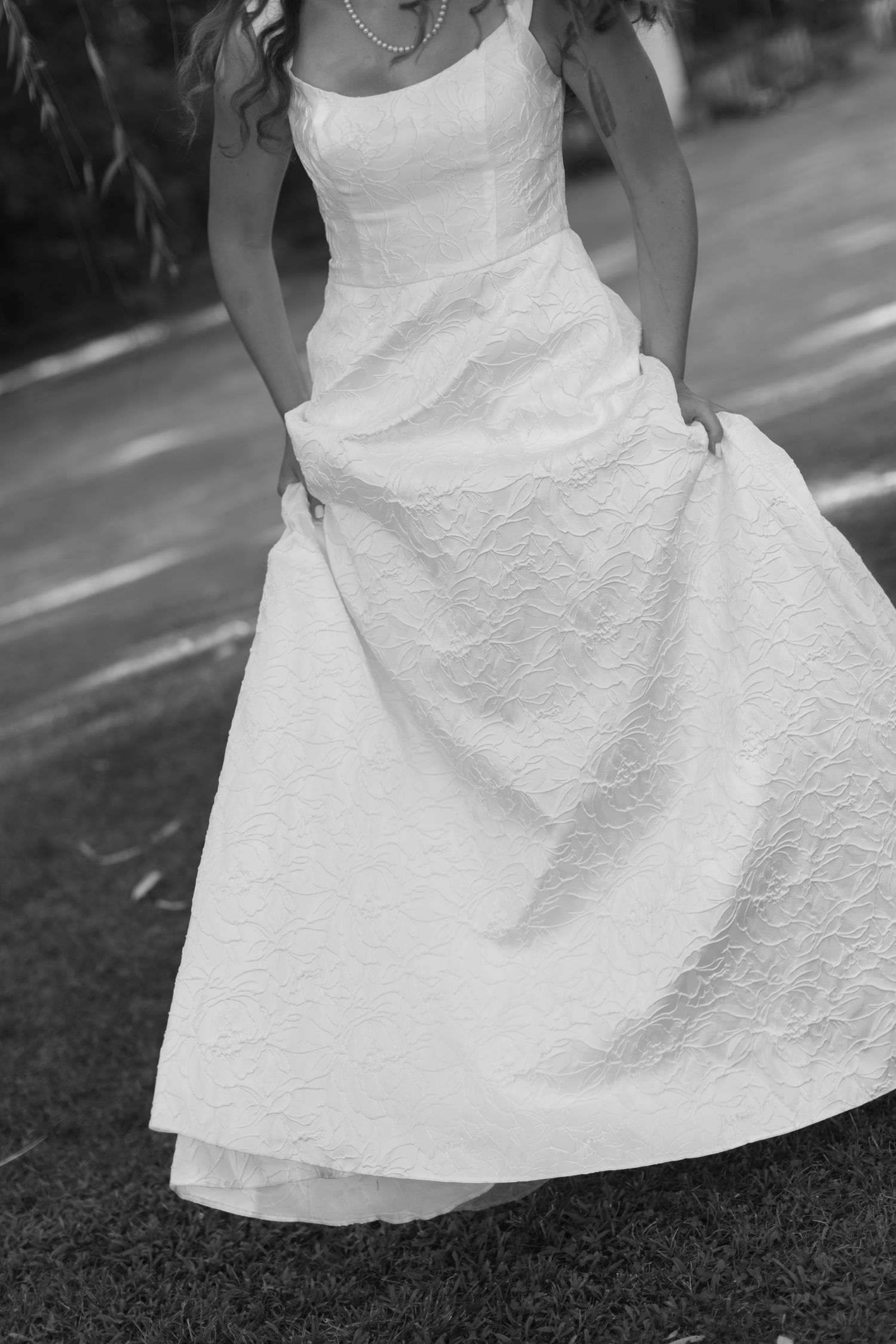Black and white photo showcasing the textured details of a white wedding dress on grass.