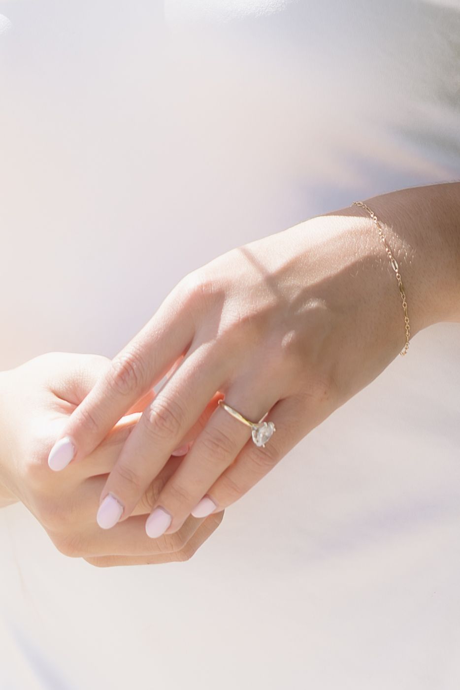 A delicate hand with manicured nails and an engagement ring is shown in soft ethereal lighting.