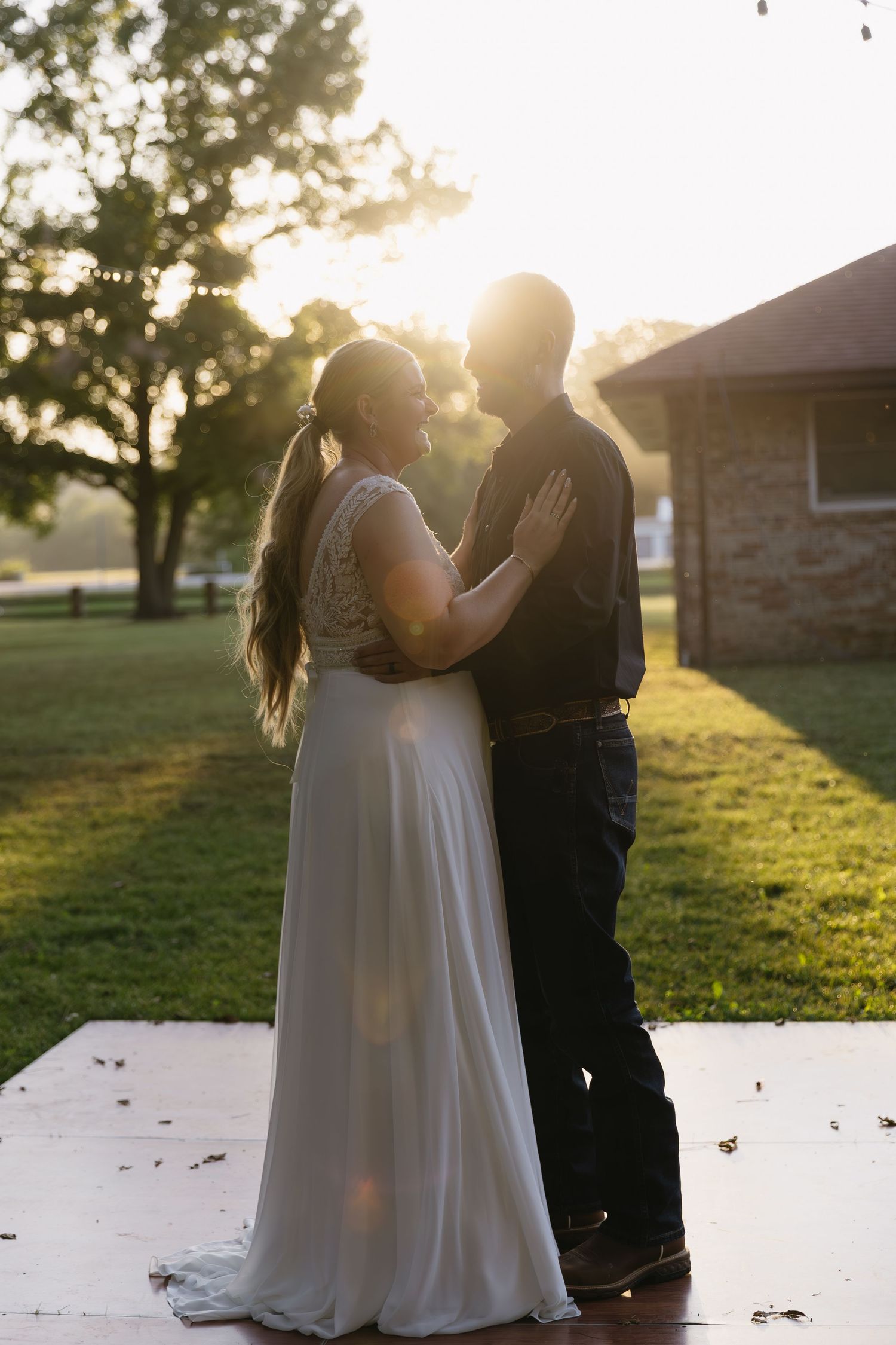 A couple embraces during sunset on their wedding day with golden light filtering through trees.