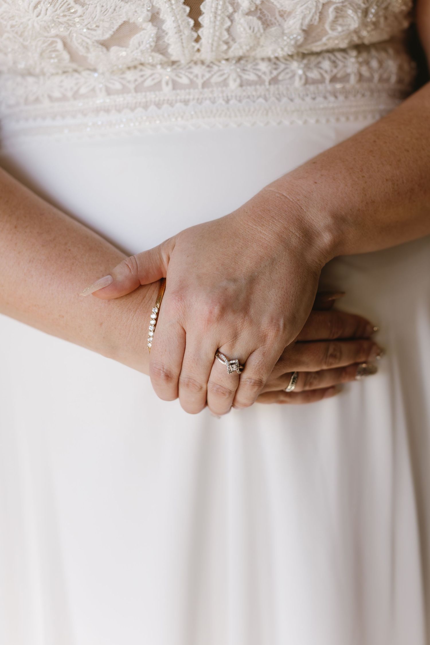 Close-up detail of hands touching the lace trim on a white wedding dress waistline.