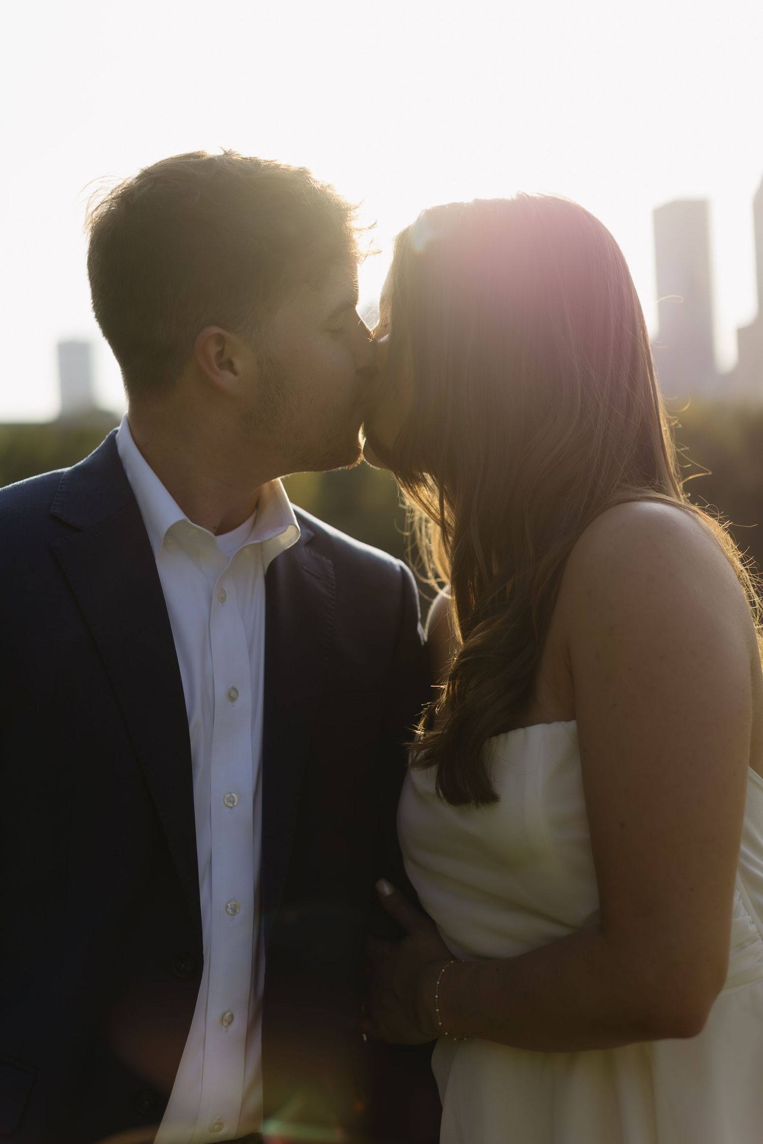 A couple shares a romantic moment at sunset with soft backlighting creating a silhouette effect.