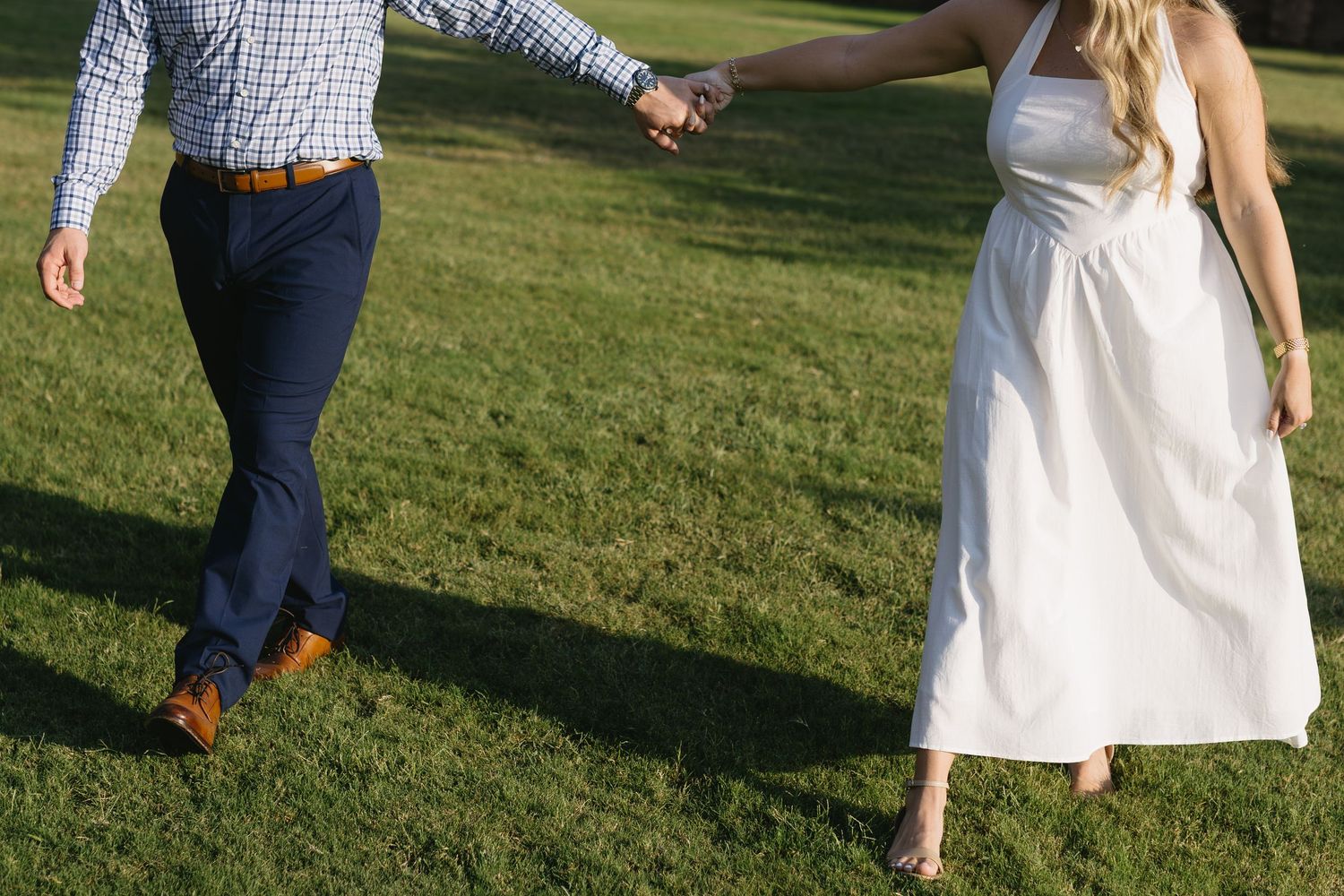 A group of people wearing formal attire walk across a green lawn during what appears to be a summer outdoor event.