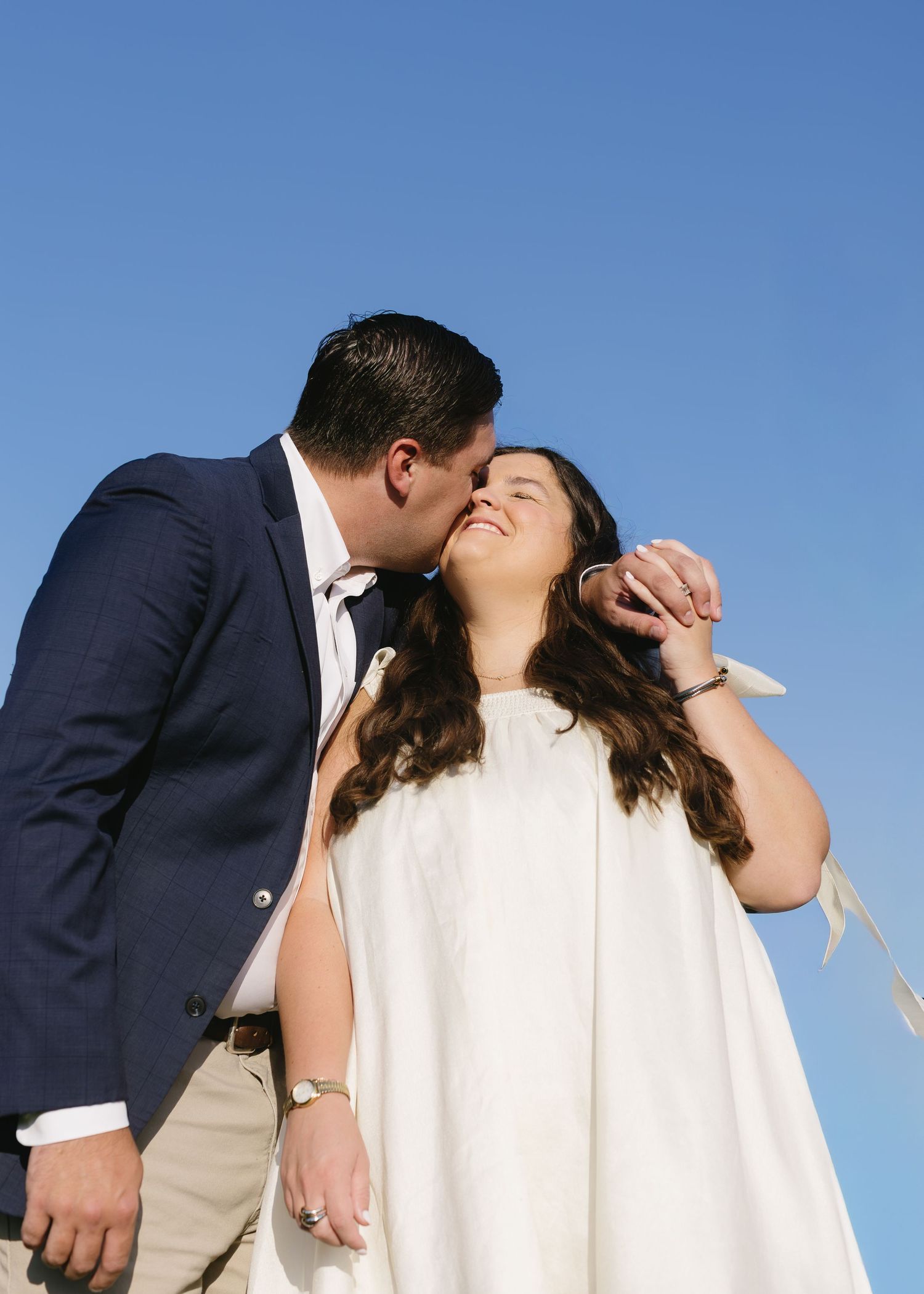 Wedding couple sharing romantic moments against bright blue sky backdrop.