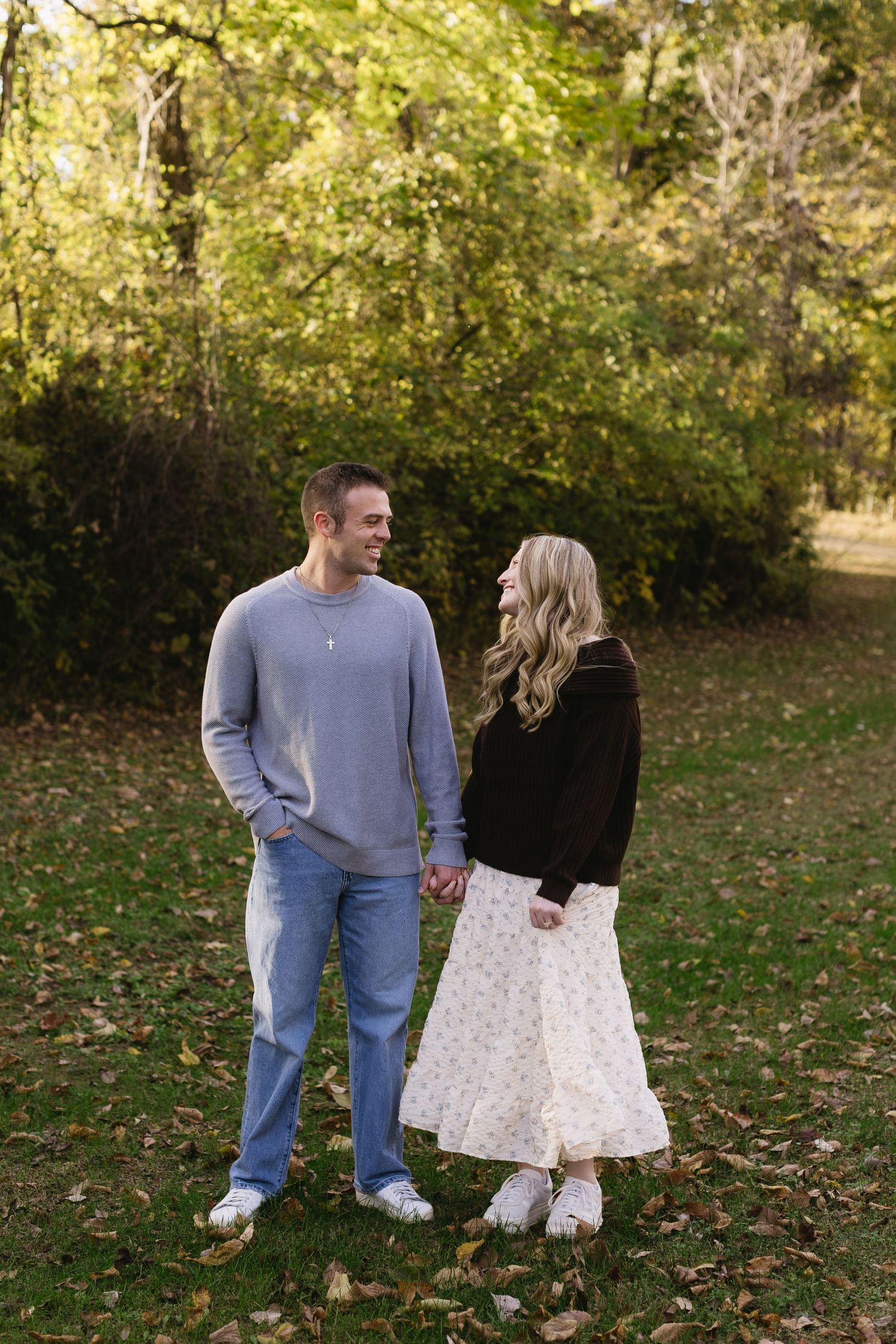 A couple shares a romantic moment in a fall setting with autumn leaves and trees in the background.