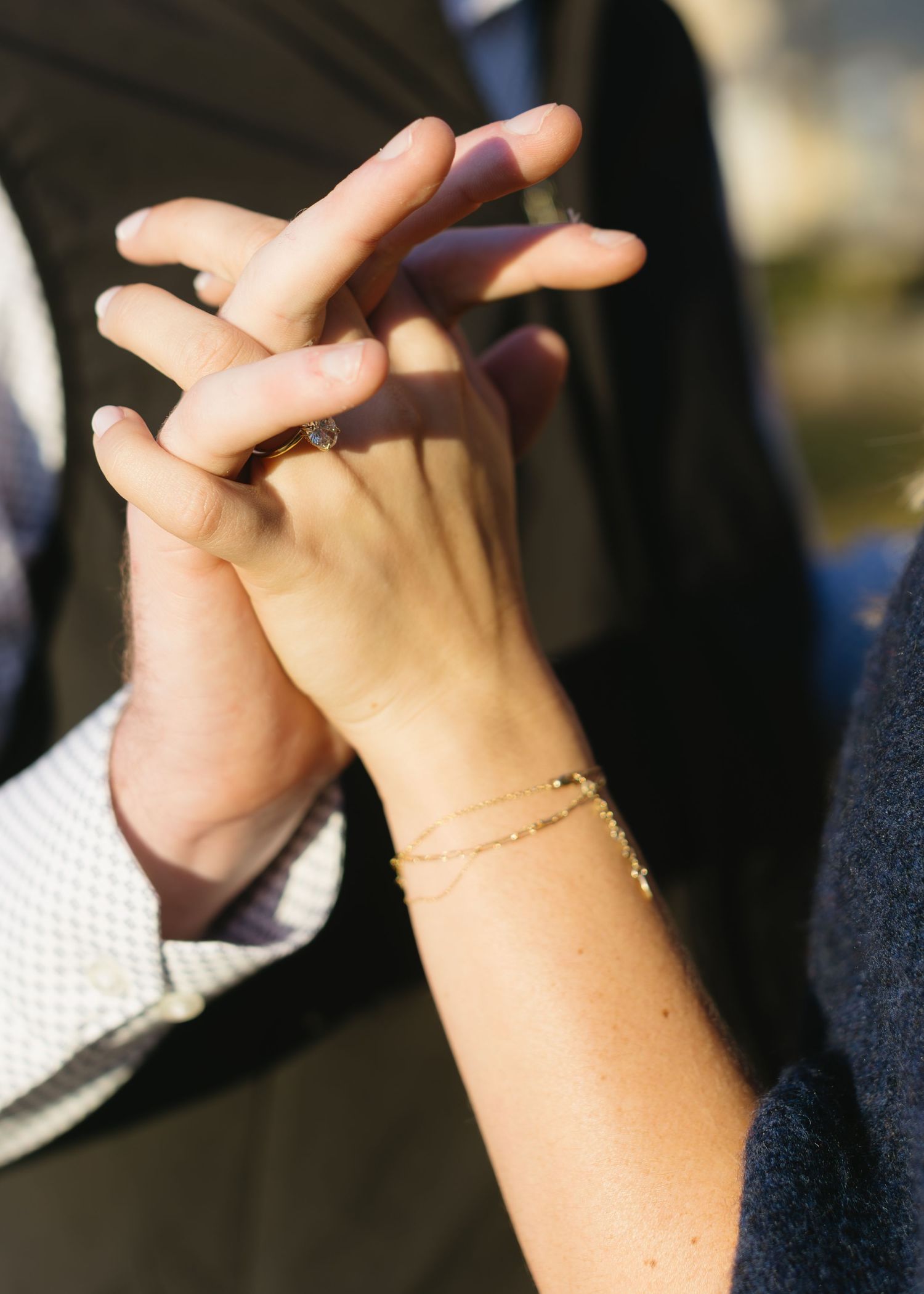 Close-up of intertwined hands with a delicate bracelet visible on one wrist in natural sunlight.