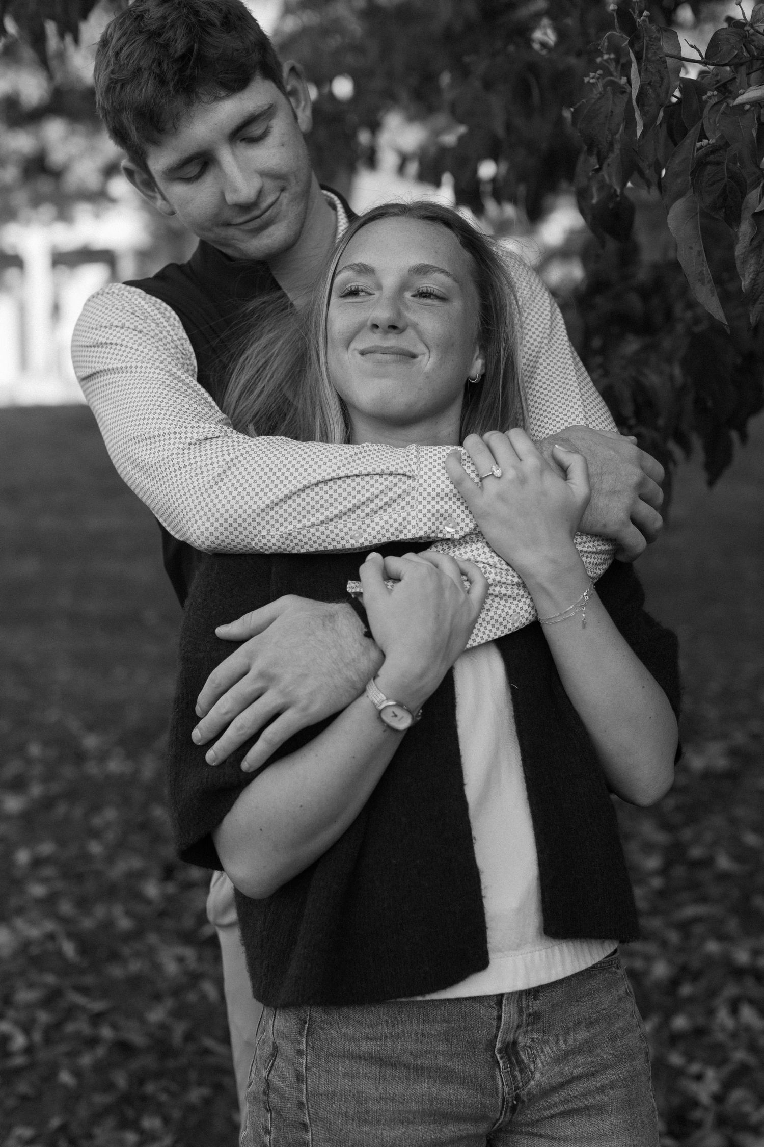A black and white portrait of a couple embracing outdoors with joyful expressions and casual attire.