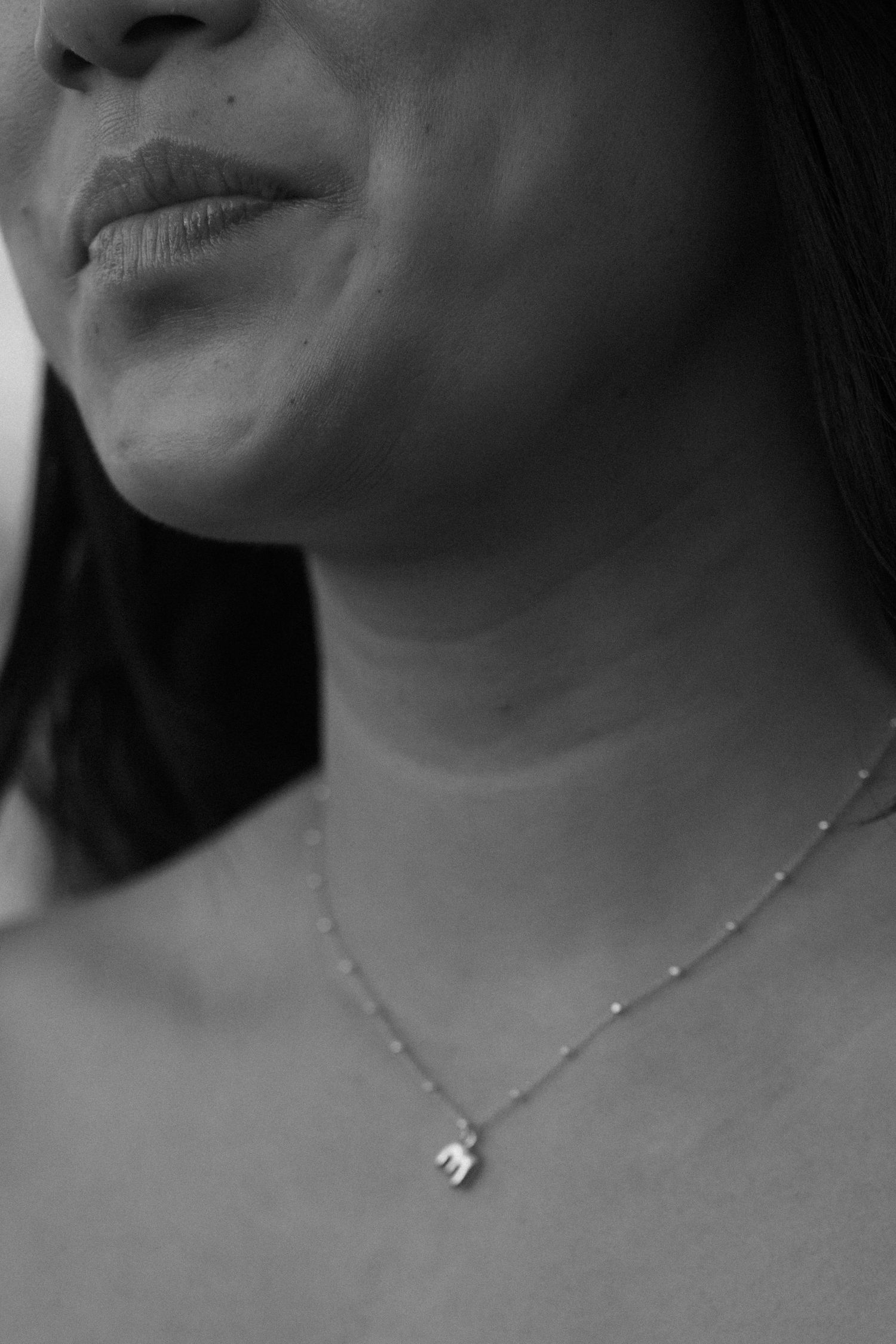 Close-up black and white profile view of neck and collarbone wearing delicate necklace.