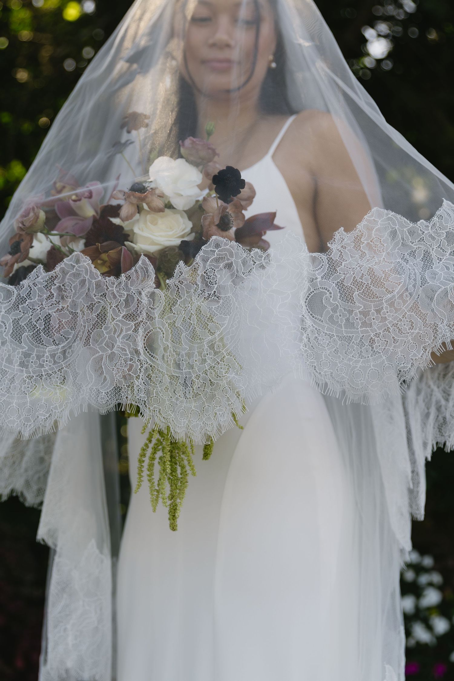 An elegant bridal veil with intricate lace detail drapes beautifully against a white wedding dress.