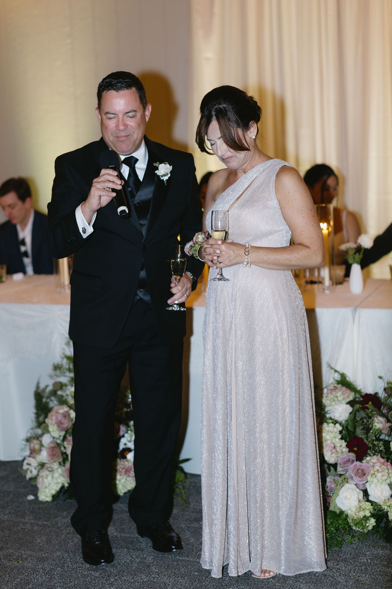 Wedding party members in formal attire giving toasts at an elegant reception.