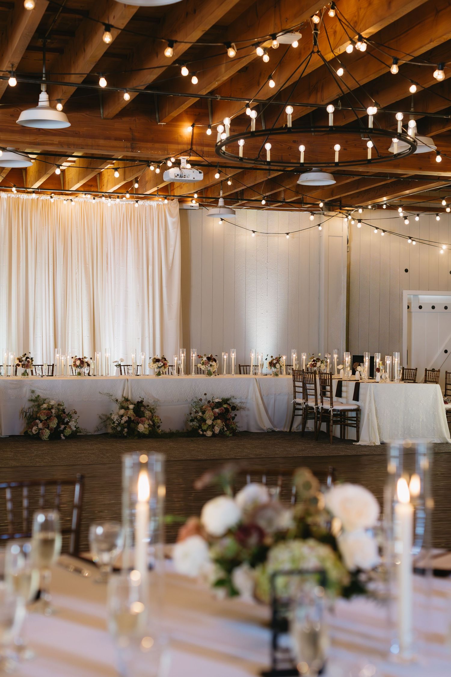 Wedding reception venue with string lights, white draping, and elegant table settings.