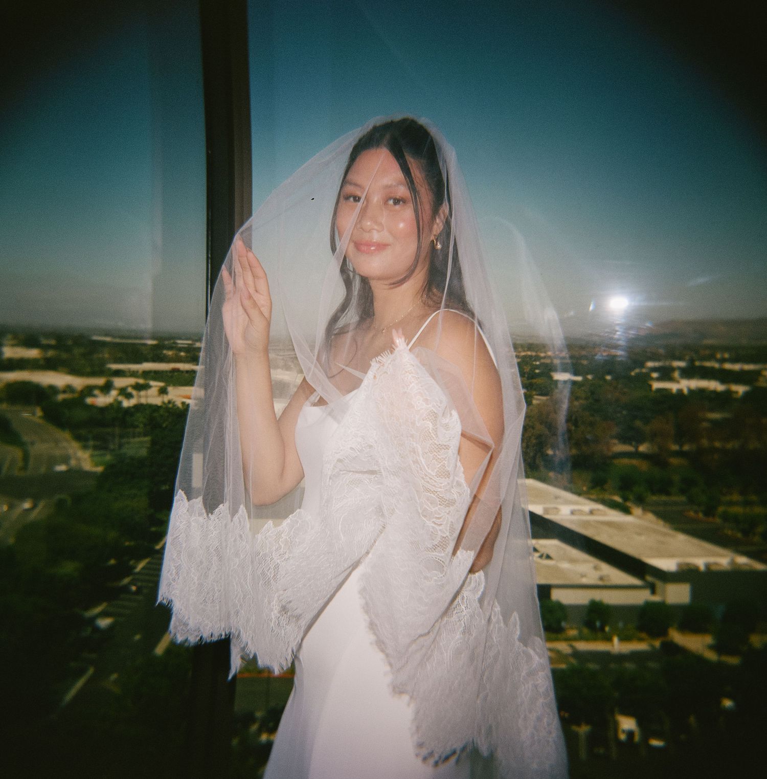 A wedding dress and veil silhouetted against a scenic city view at sunset.