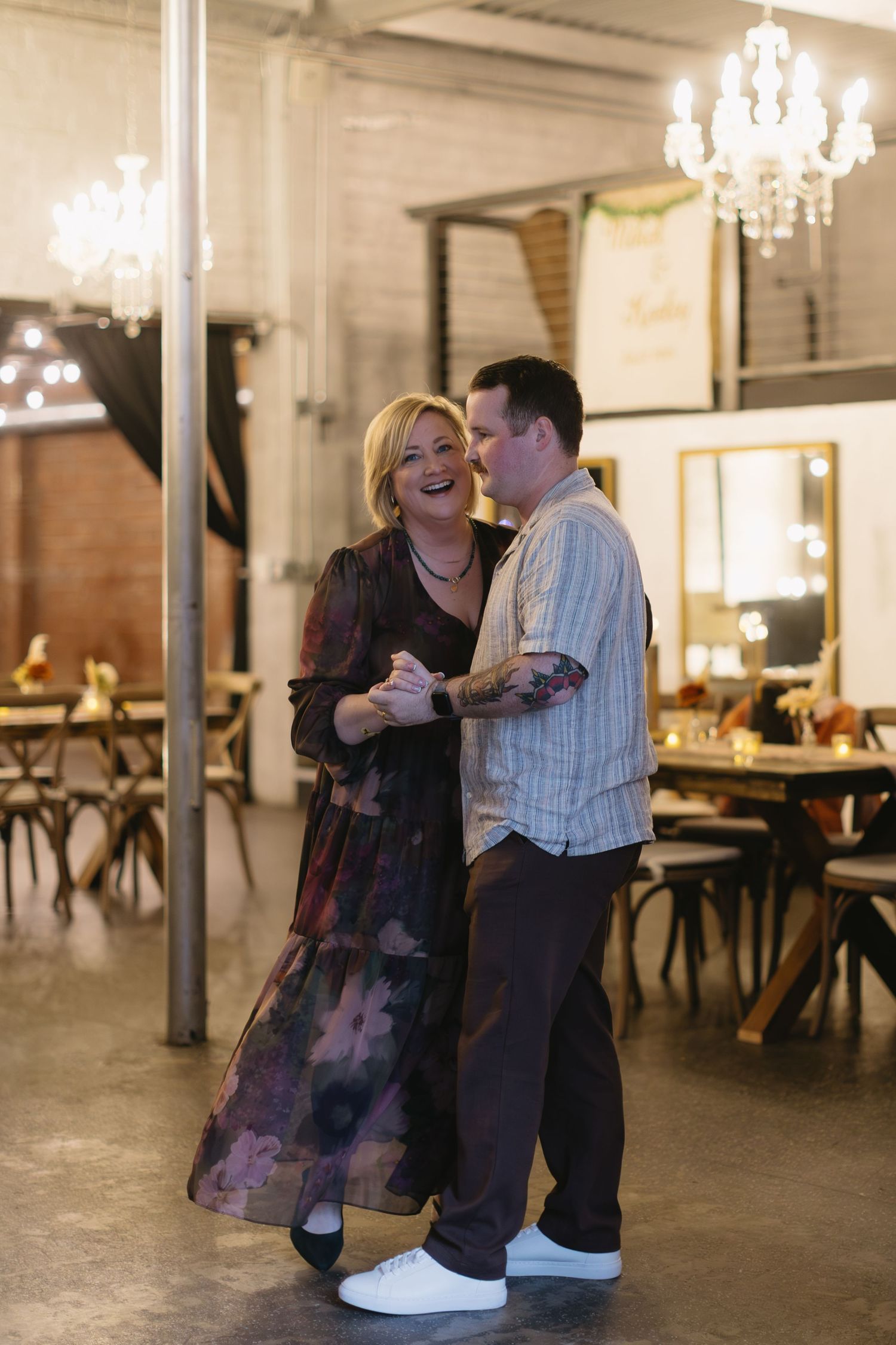Couple dancing together in an industrial-style venue with chandeliers.
